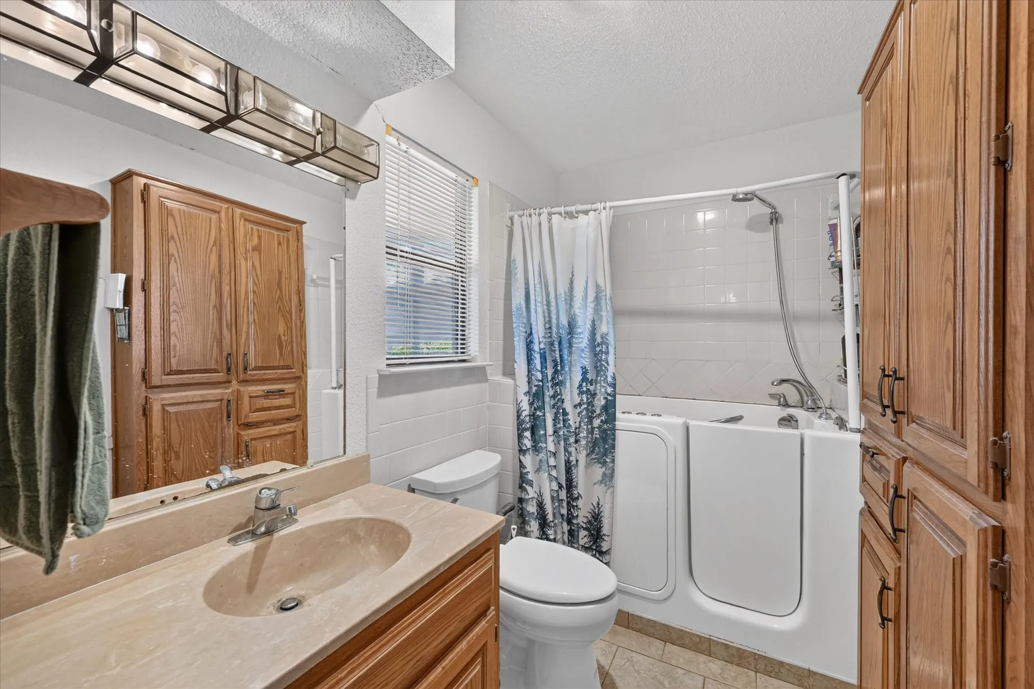 Walk-in tub with shower, vanity with integrated sink, wood-finish cabinetry, and tiled flooring