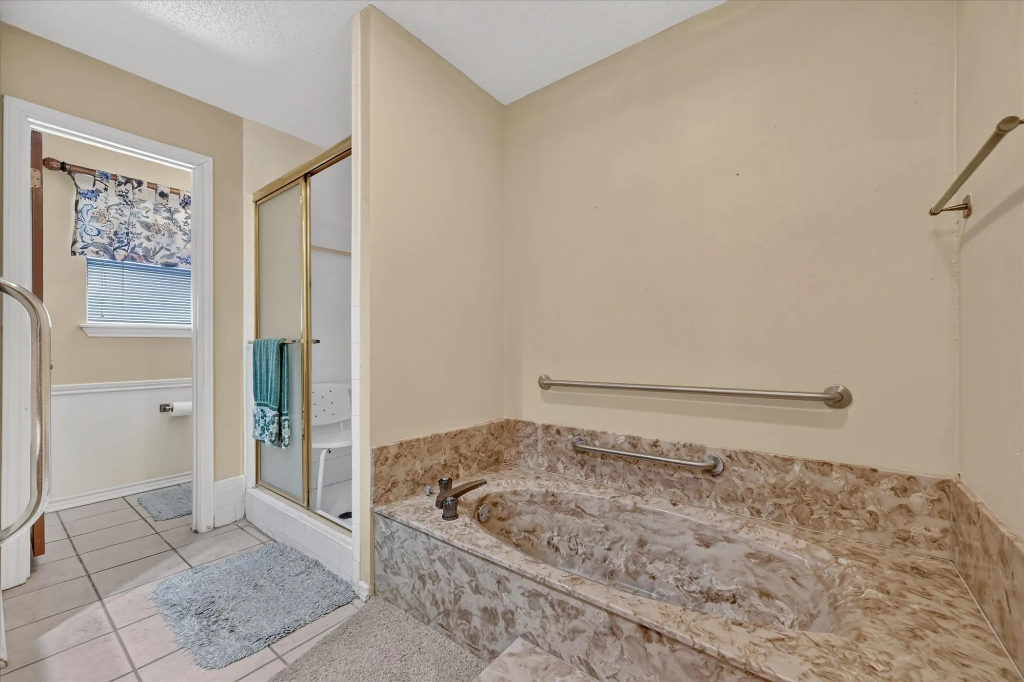 Jetted soaking tub with stone surround, separate shower enclosure with sliding glass door, and tiled flooring