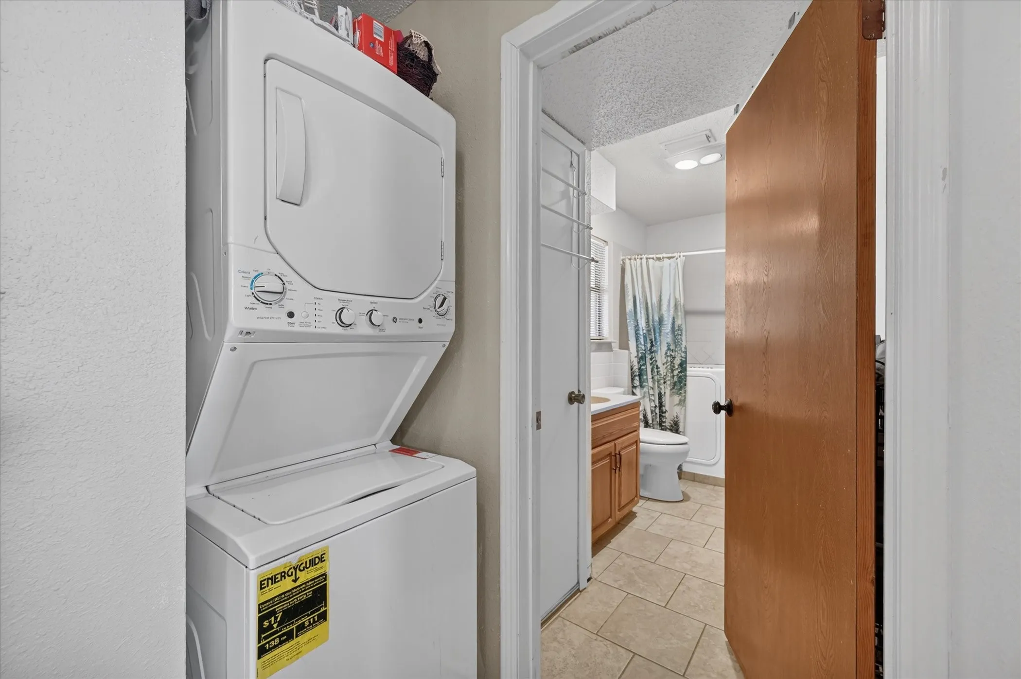 Stackable washer and dryer unit, and a bathroom featuring a wood-finish vanity, white sink, and tiled flooring