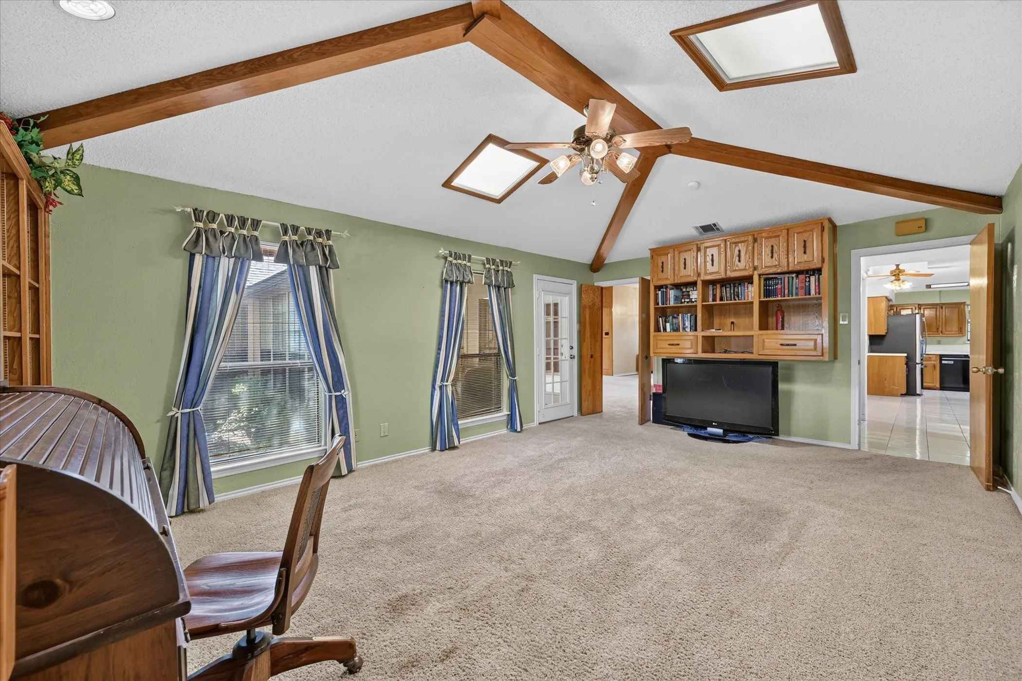 Vaulted ceiling with exposed wood beams, dual skylights, and a ceiling fan