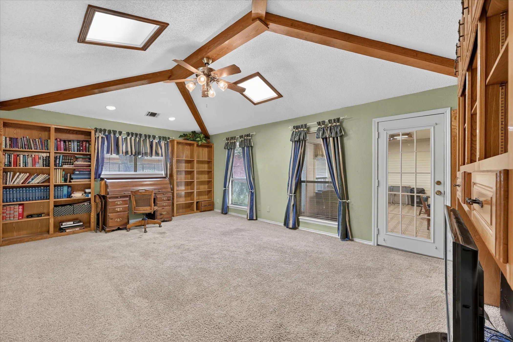 Vaulted ceiling with exposed wood beams, dual skylights, and ceiling fan