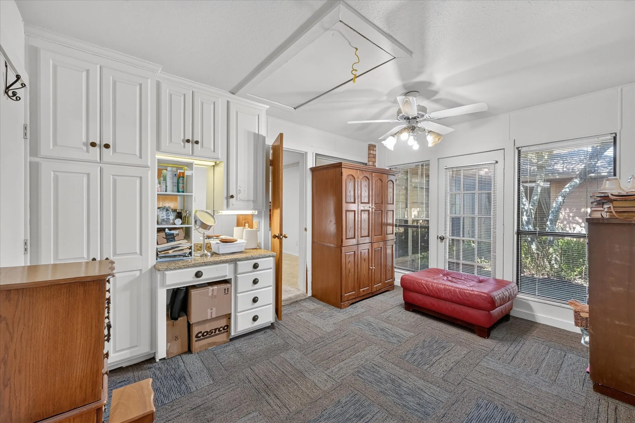 Built-in white cabinetry with a vanity area, ceiling fan with light fixture, large windows, and a glass-paneled door