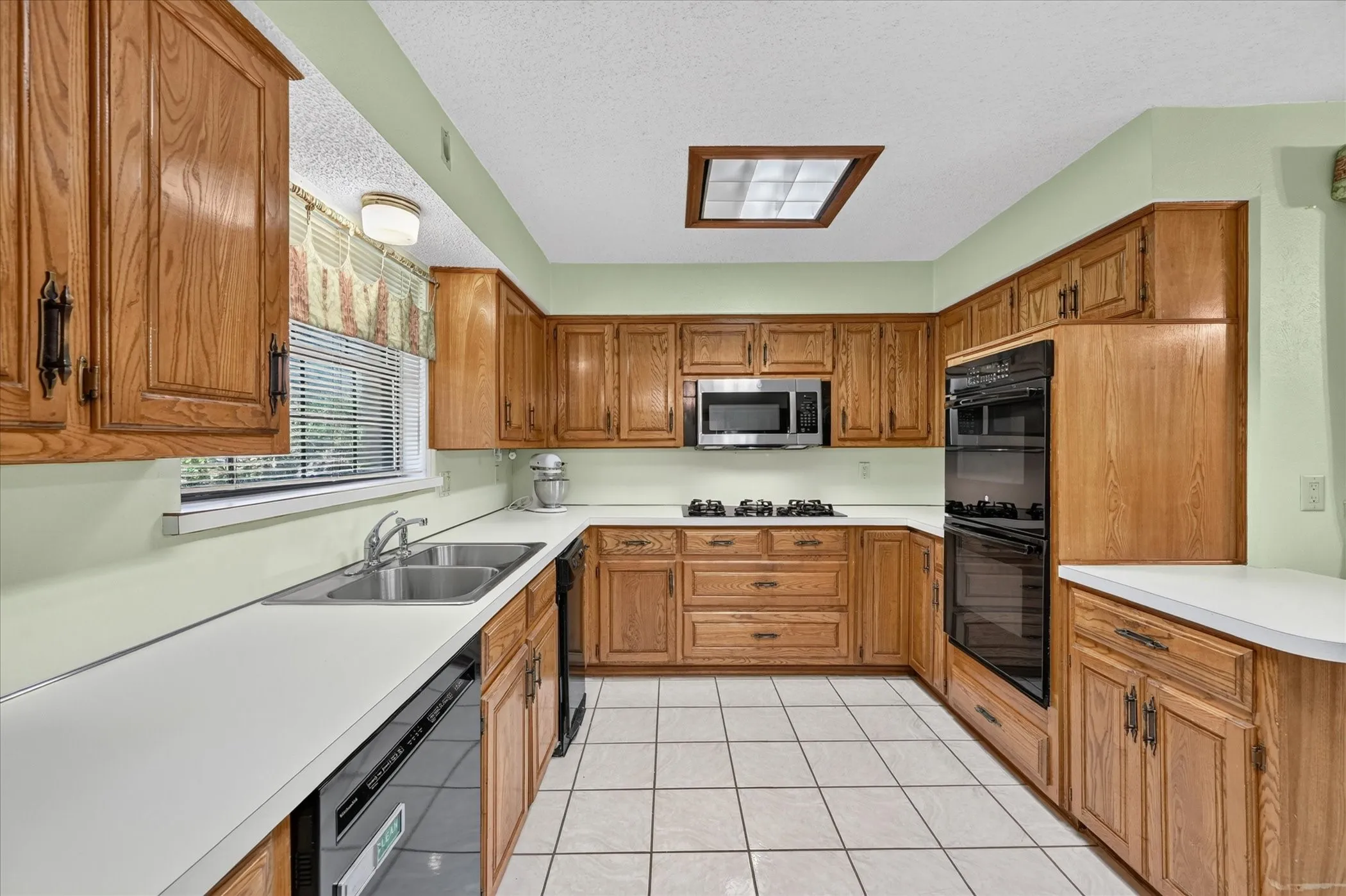 U-shaped kitchen featuring wood-finish cabinetry, white countertops, a double basin stainless steel sink, a built-in double oven, and tiled flooring
