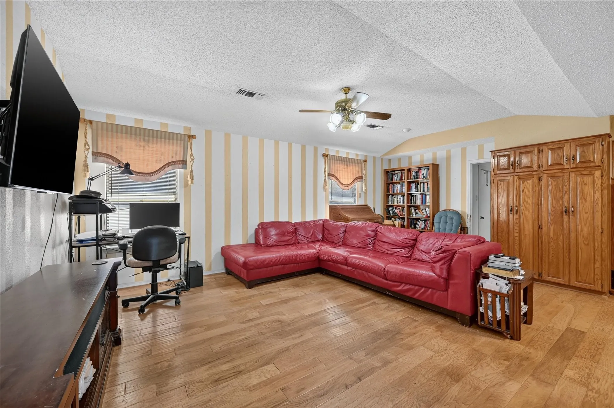 Wood-finish flooring, built-in wooden cabinetry, a built-in ceiling fan, and window treatments