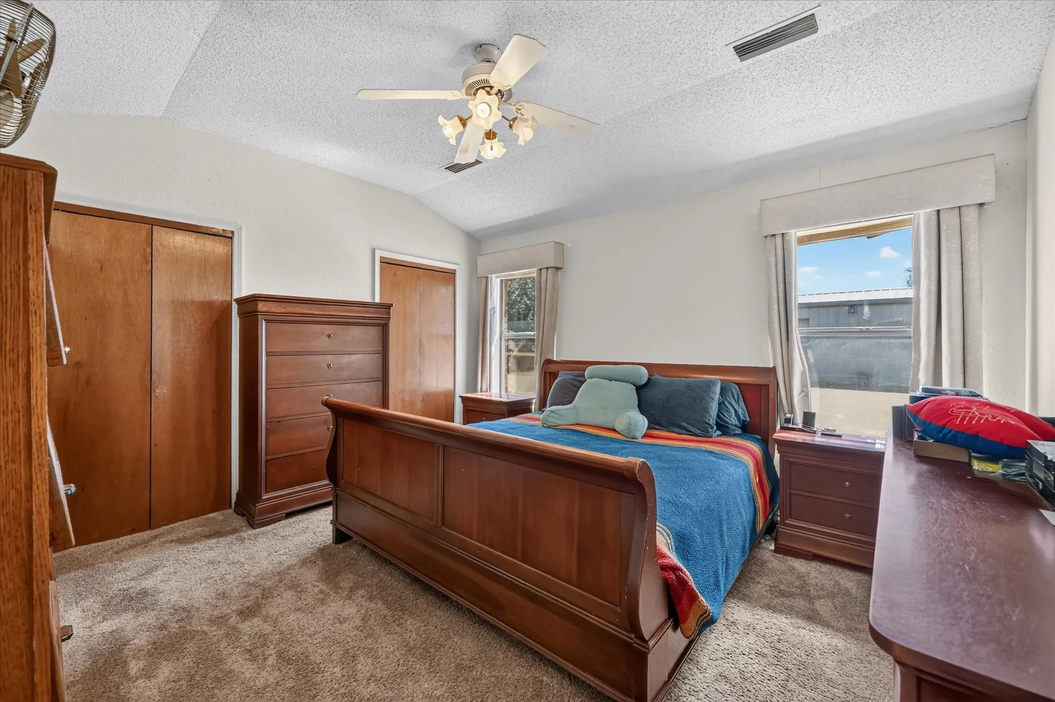 Vaulted ceiling with a ceiling fan light fixture, two windows, two wood-finish bi-fold closet doors, and carpeted flooring