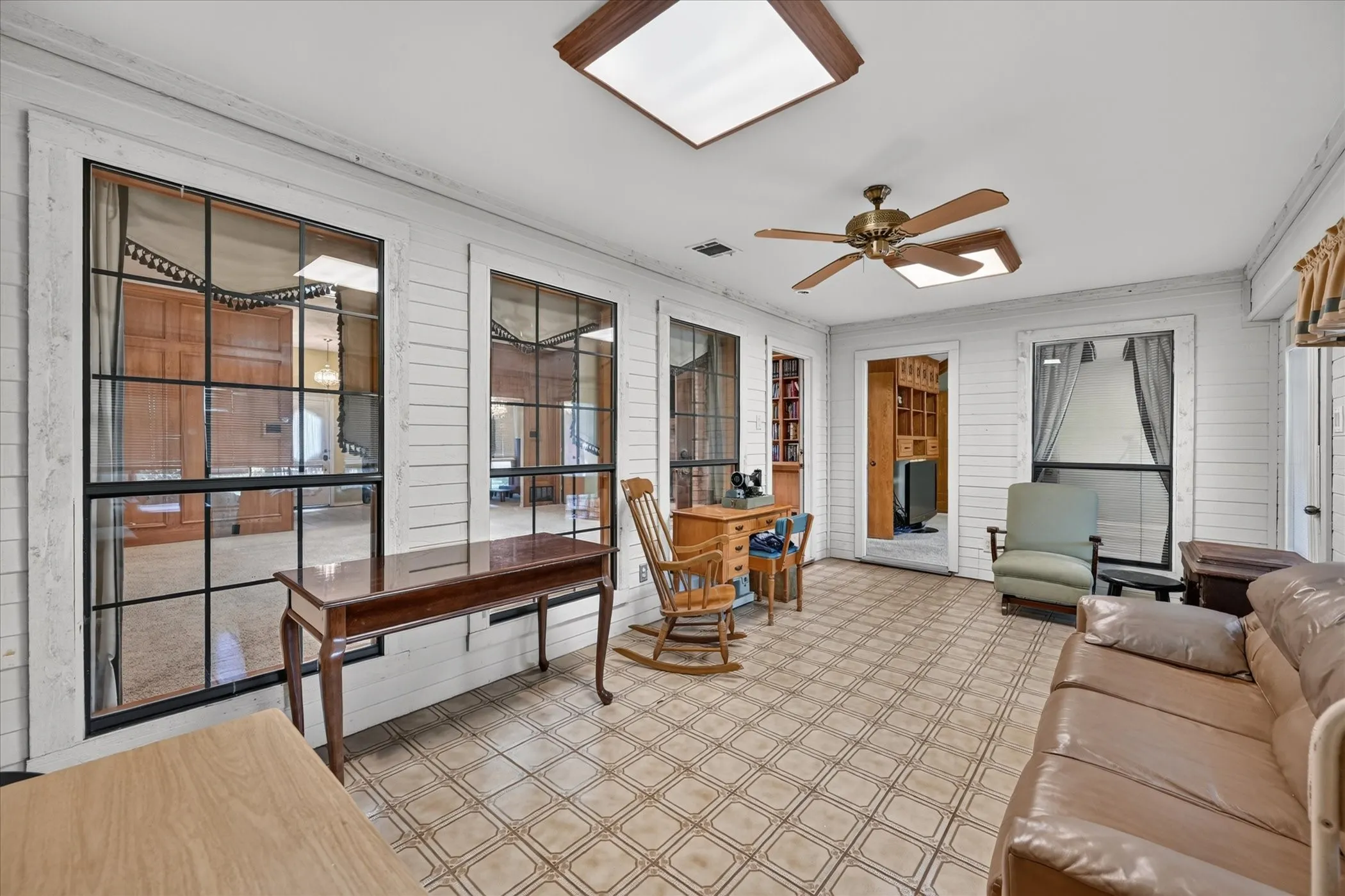 Enclosed sunroom featuring multiple large windows, patterned tile flooring, and a ceiling fan with integrated lighting