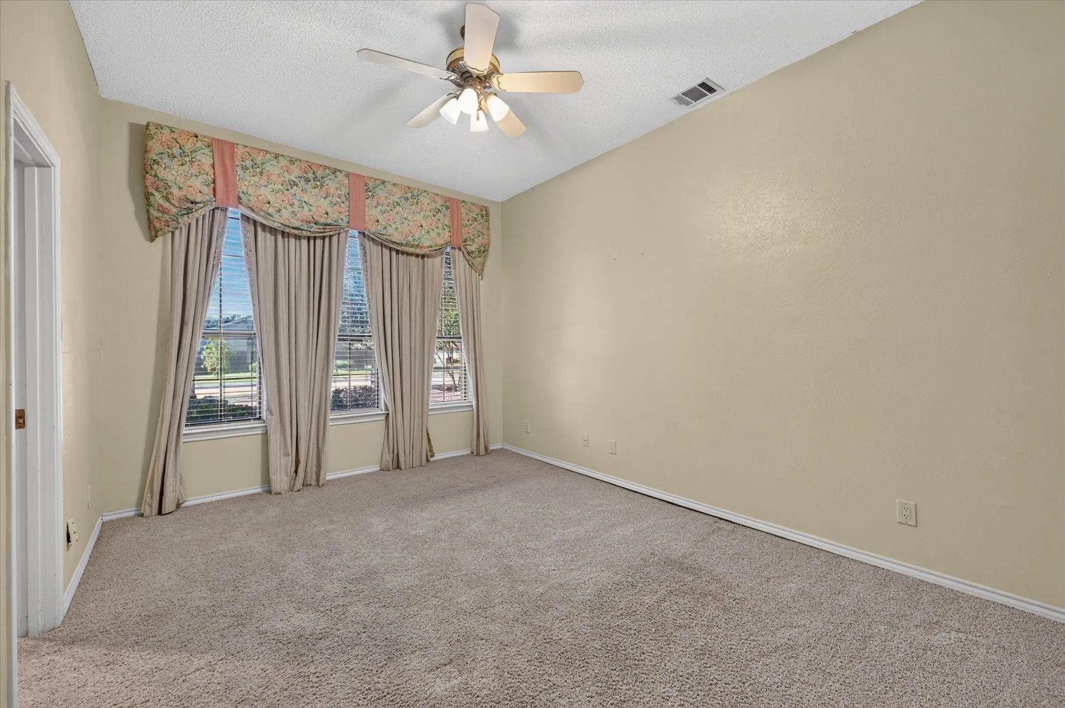 Sloped ceiling room featuring a ceiling fan with integrated lighting, broad window treatments, and neutral carpeting