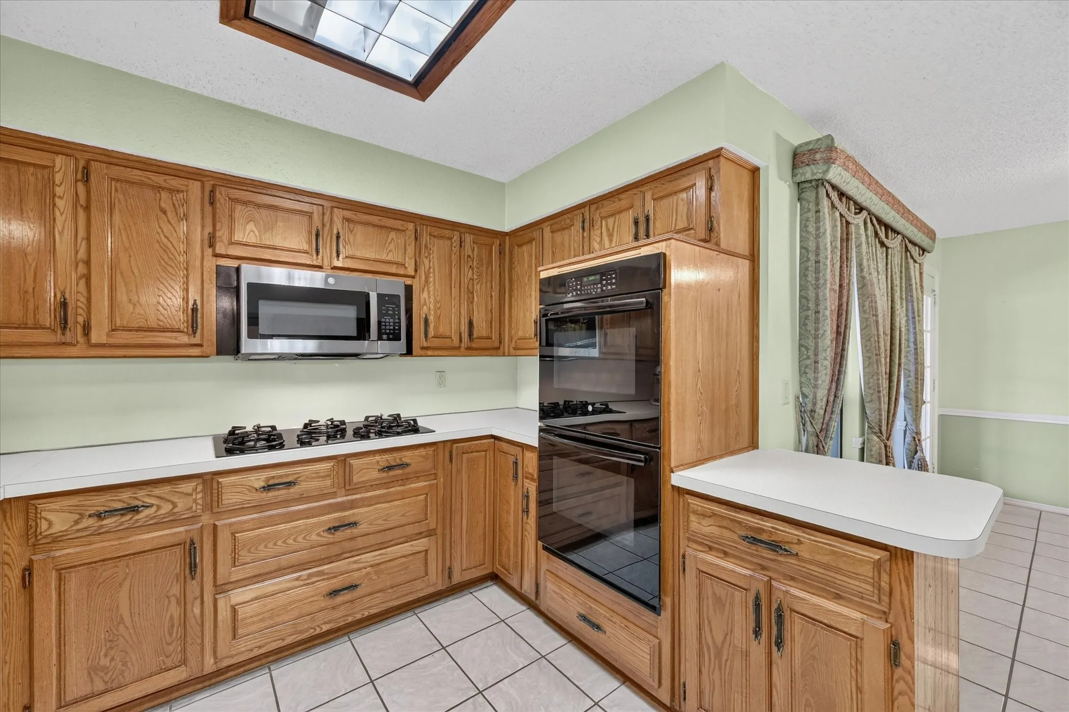 Kitchen featuring wood cabinetry, white countertops, built-in stainless steel microwave, gas cooktop, and tile flooring