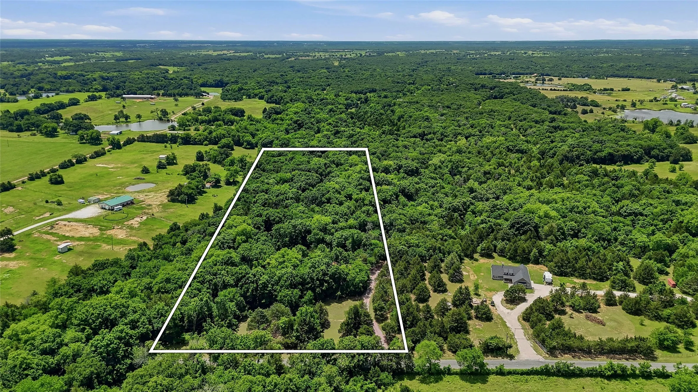 Expansive wooded lot with mature trees, surrounded by lush green landscapes