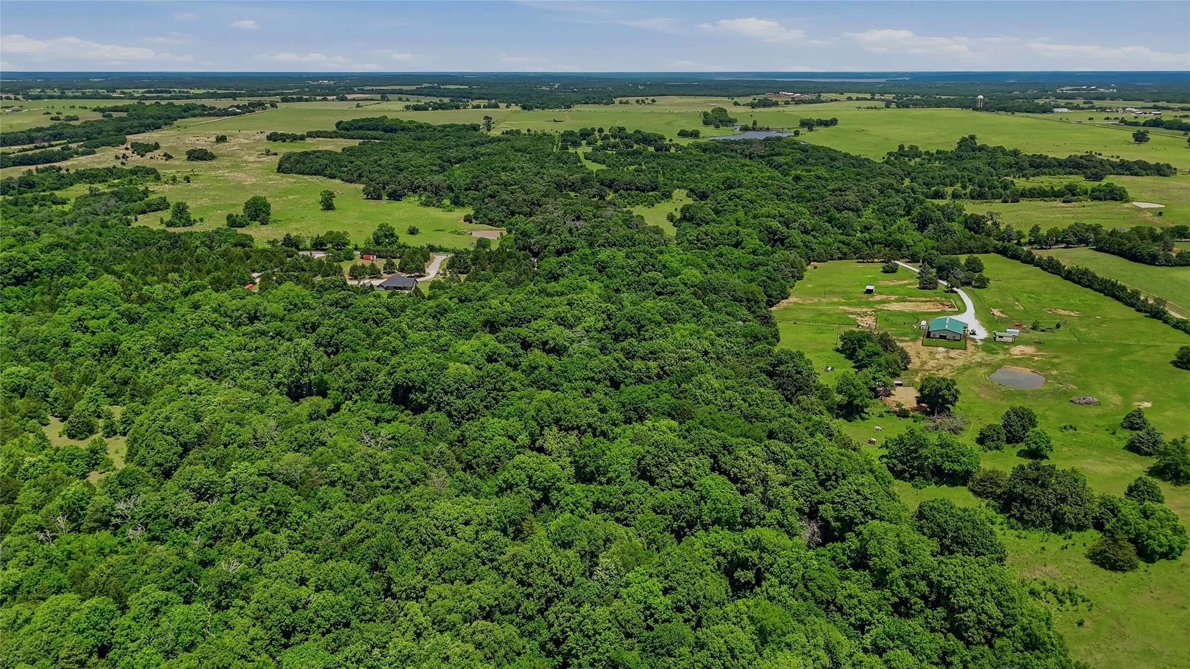 Expansive acreage featuring mature trees, open green spaces, and a visible structure with a green roof
