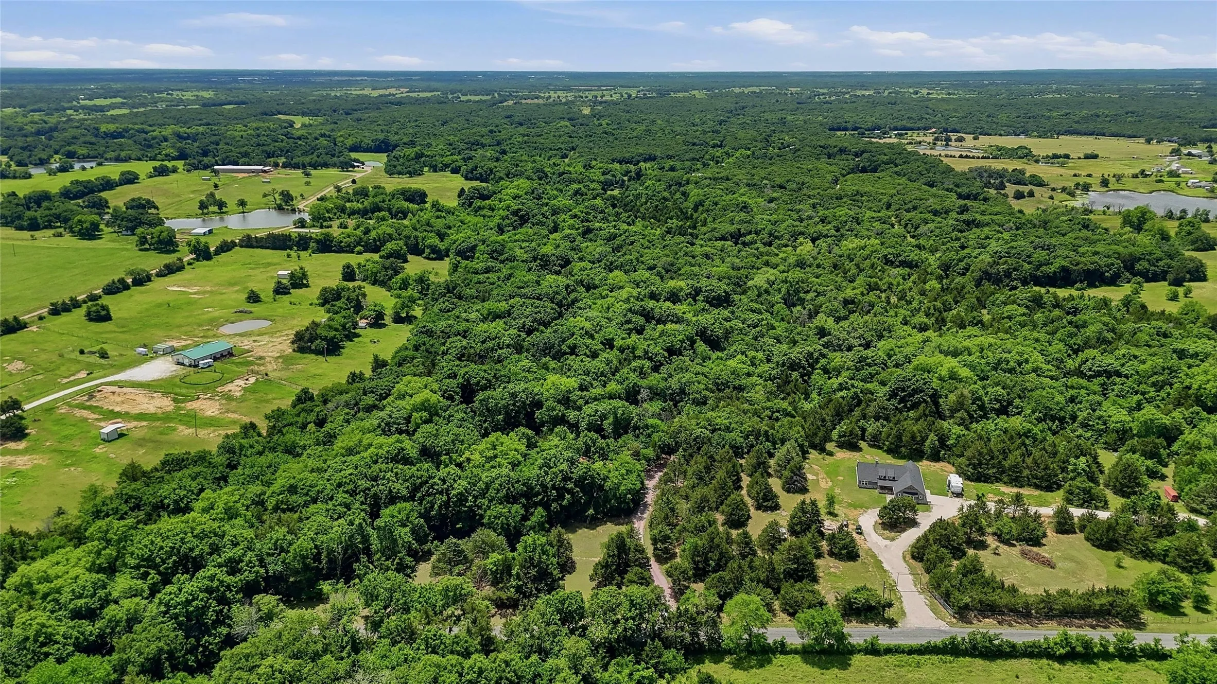 Expansive property featuring dense tree coverage, open grassy areas, and multiple bodies of water