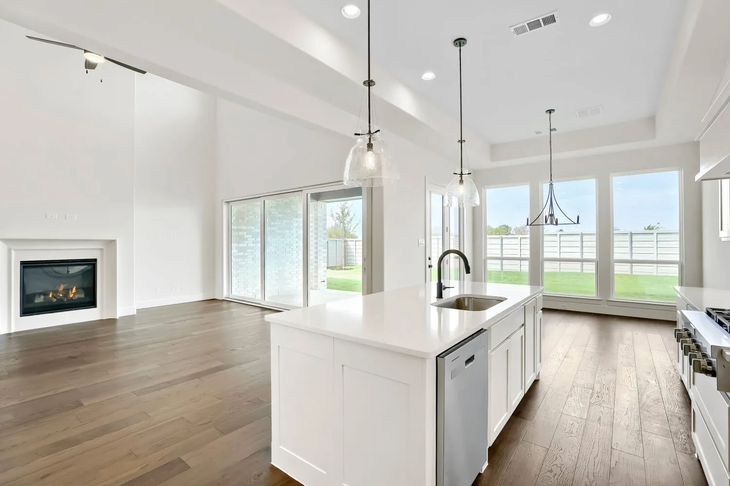 Open-concept living space featuring wood-finish flooring, a contemporary fireplace, and a kitchen island with sink
