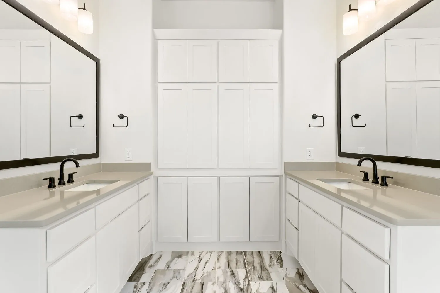 Dual vanities with integrated sinks, light-toned countertops, extensive white cabinetry, large framed mirrors, and patterned floor tile