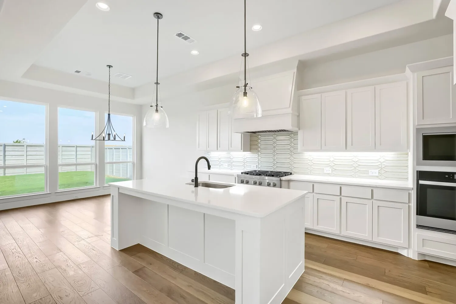 Spacious kitchen featuring an expansive island with a sink, stainless steel appliances, wood-finish flooring, and a tray ceiling