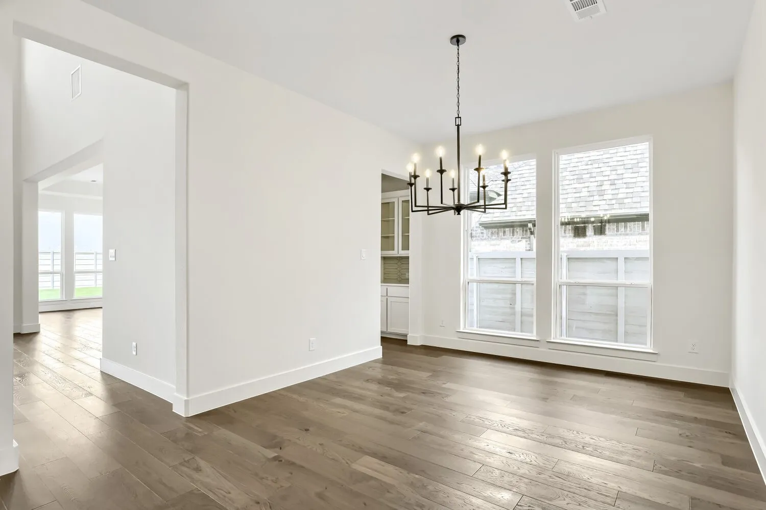 Wood-finish flooring, white walls, and a black chandelier