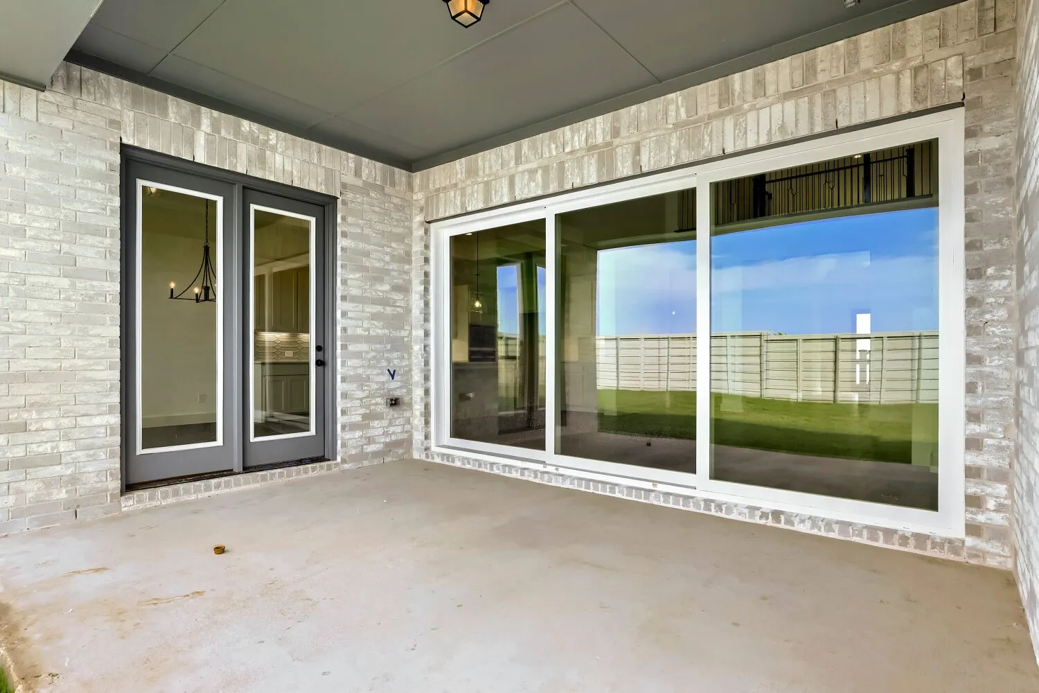 Covered patio with a concrete surface, featuring brick exterior walls, dual French doors, and large sliding glass doors