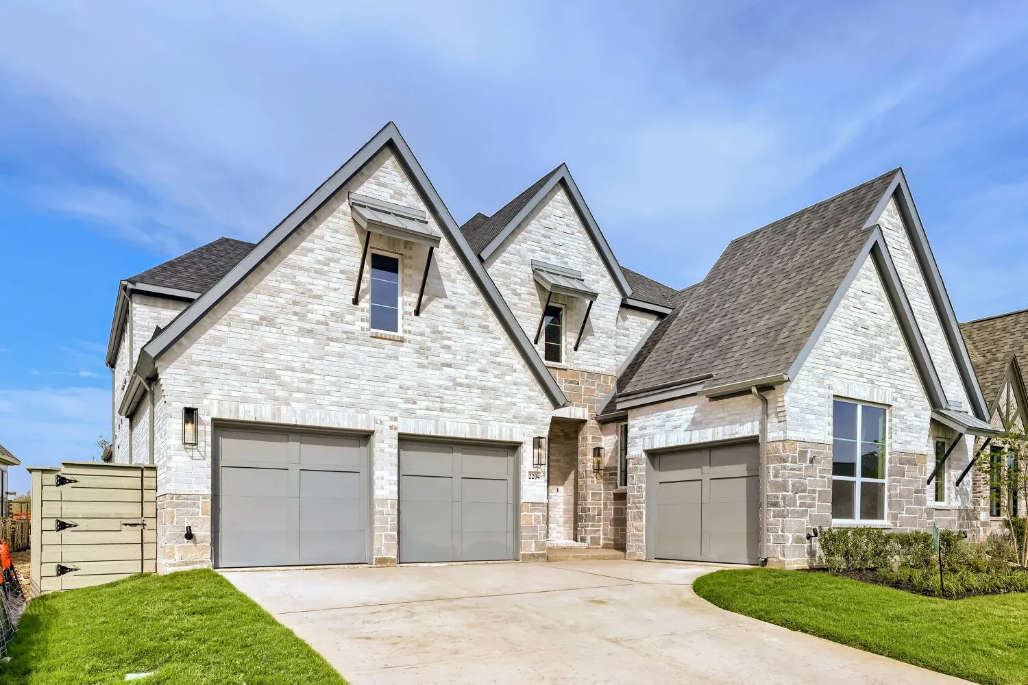White brick exterior with stone accents, a three-car garage, dark shingle roofing, and an arched entry