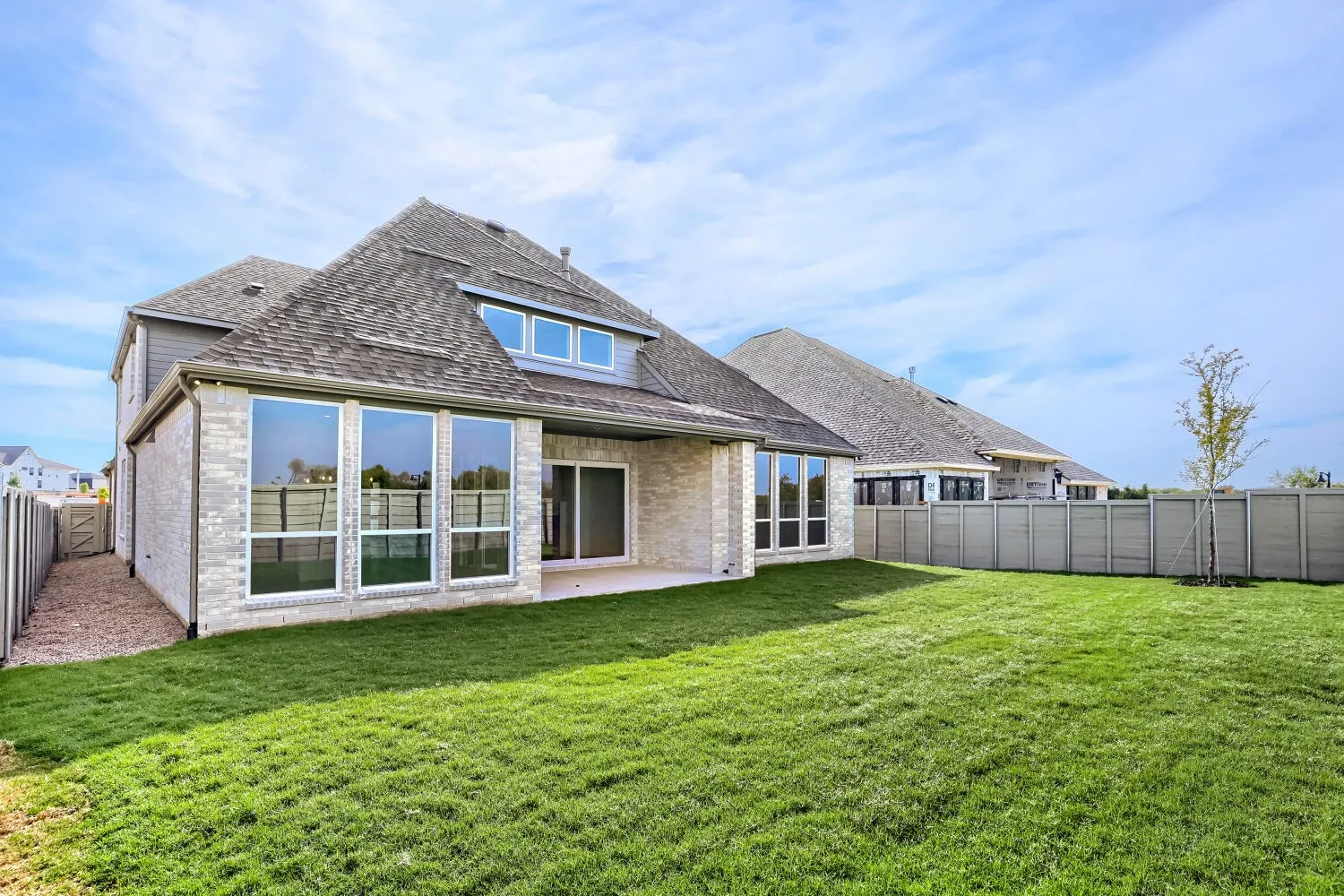 Expansive green lawn, light brick exterior, large pane windows, sliding glass door, and a private perimeter fence