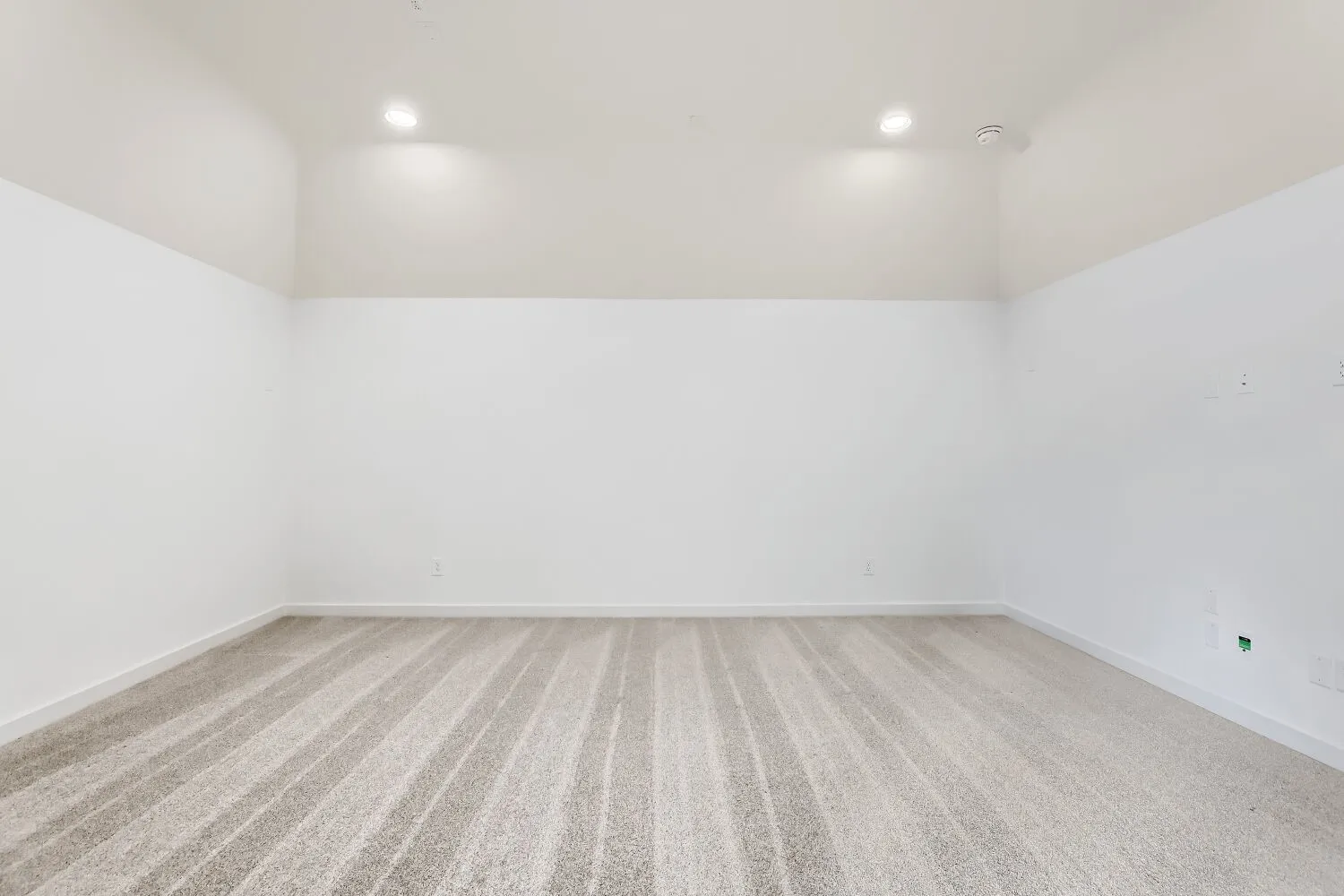 Vaulted ceiling with recessed lighting and neutral-toned carpeting