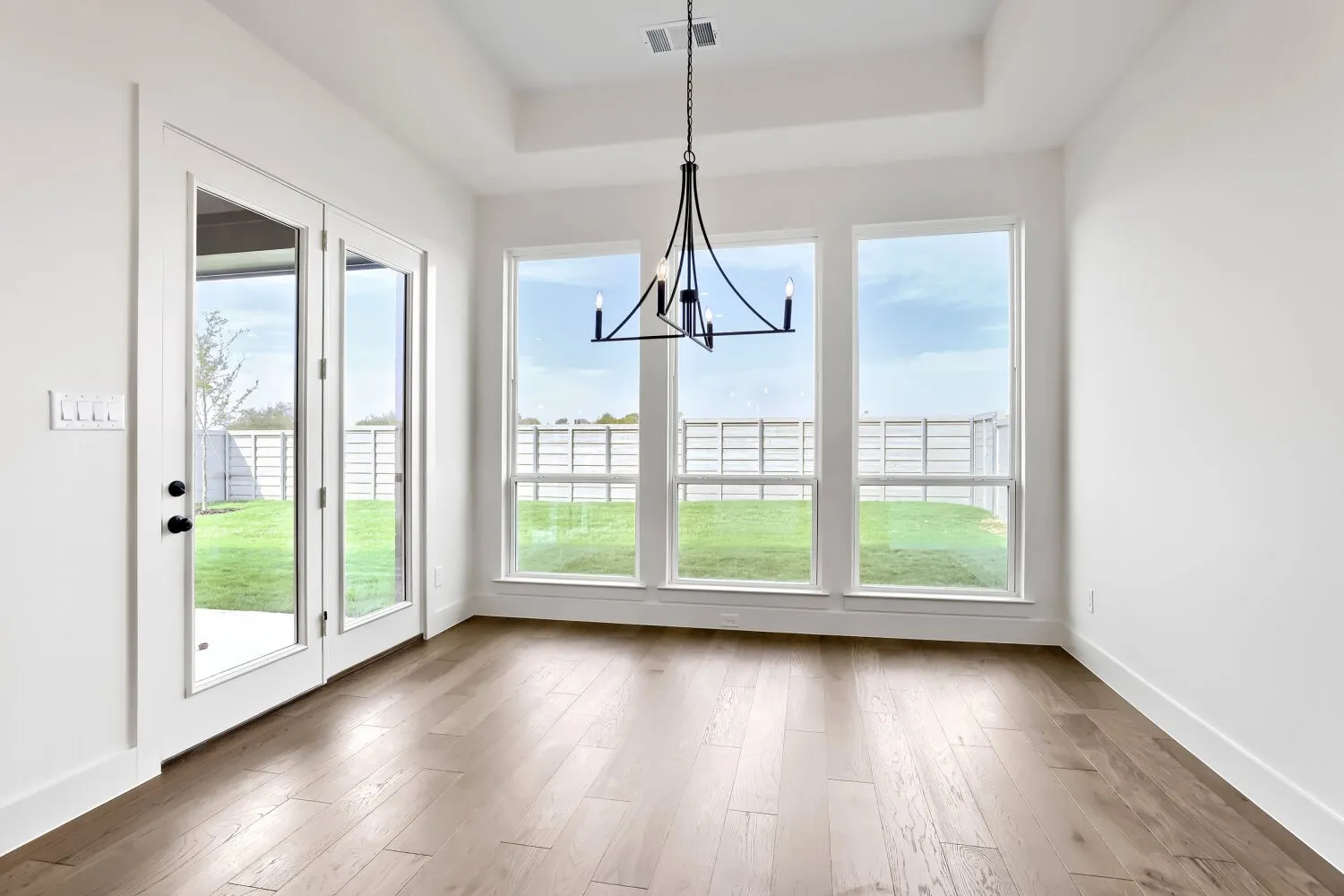 Tray ceiling, wood-finish flooring, full-light French doors, three large windows, and a chandelier with a matte black finish