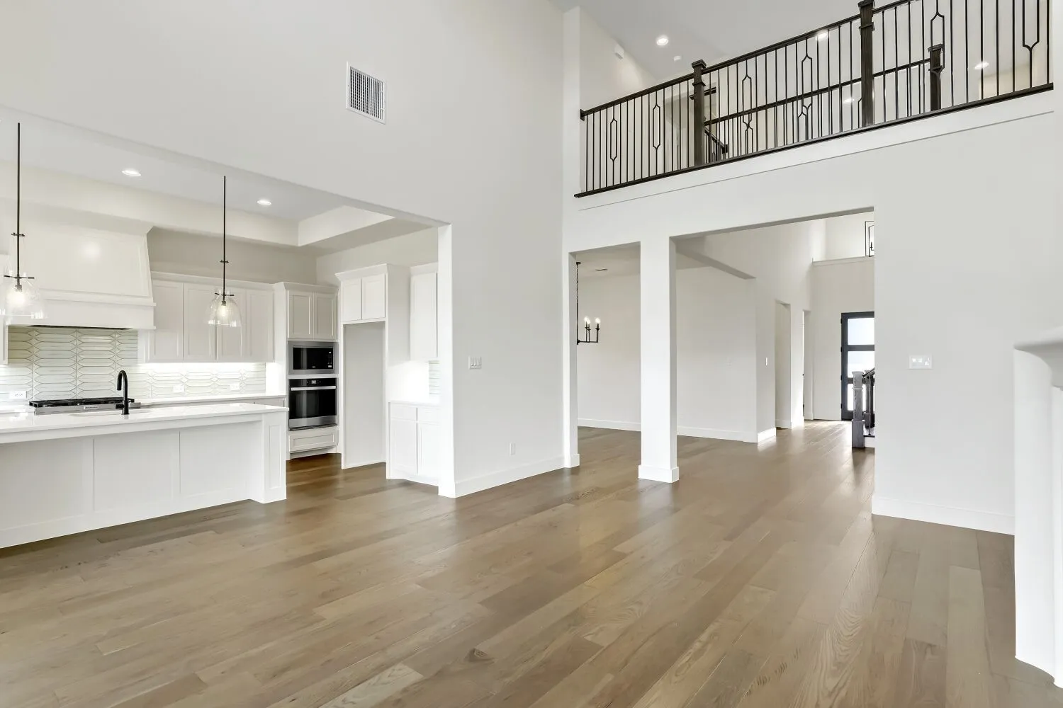 Expansive living area with wood-finish flooring, high ceilings, and a second-story balcony featuring an iron railing