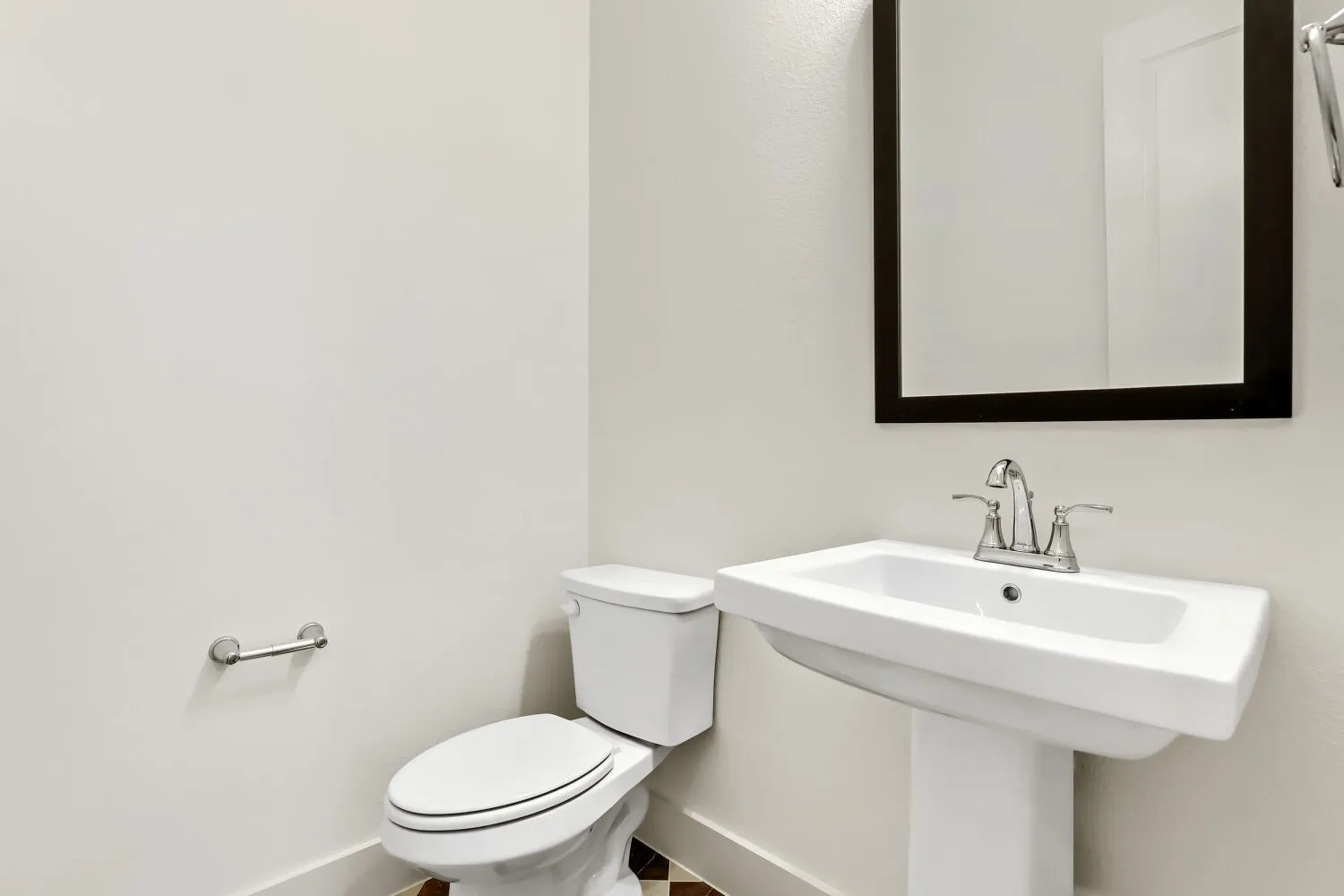 Pedestal sink with chrome faucet, framed mirror, and white toilet