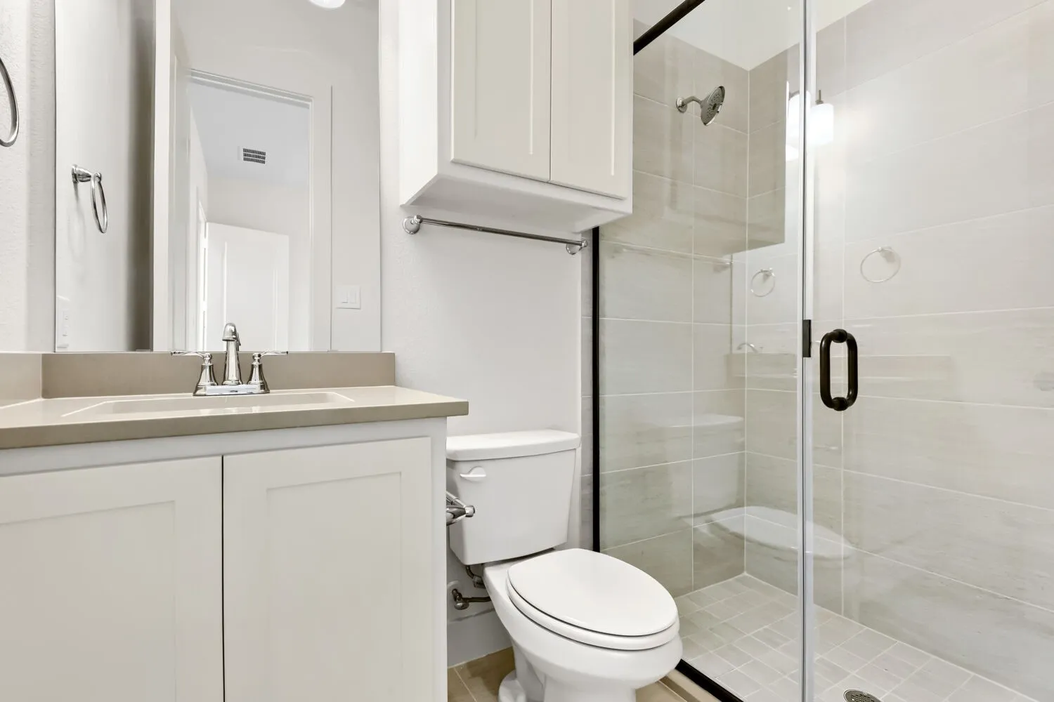 Frameless glass shower enclosure with a dark-framed door, tile flooring, and light-toned wall tiling