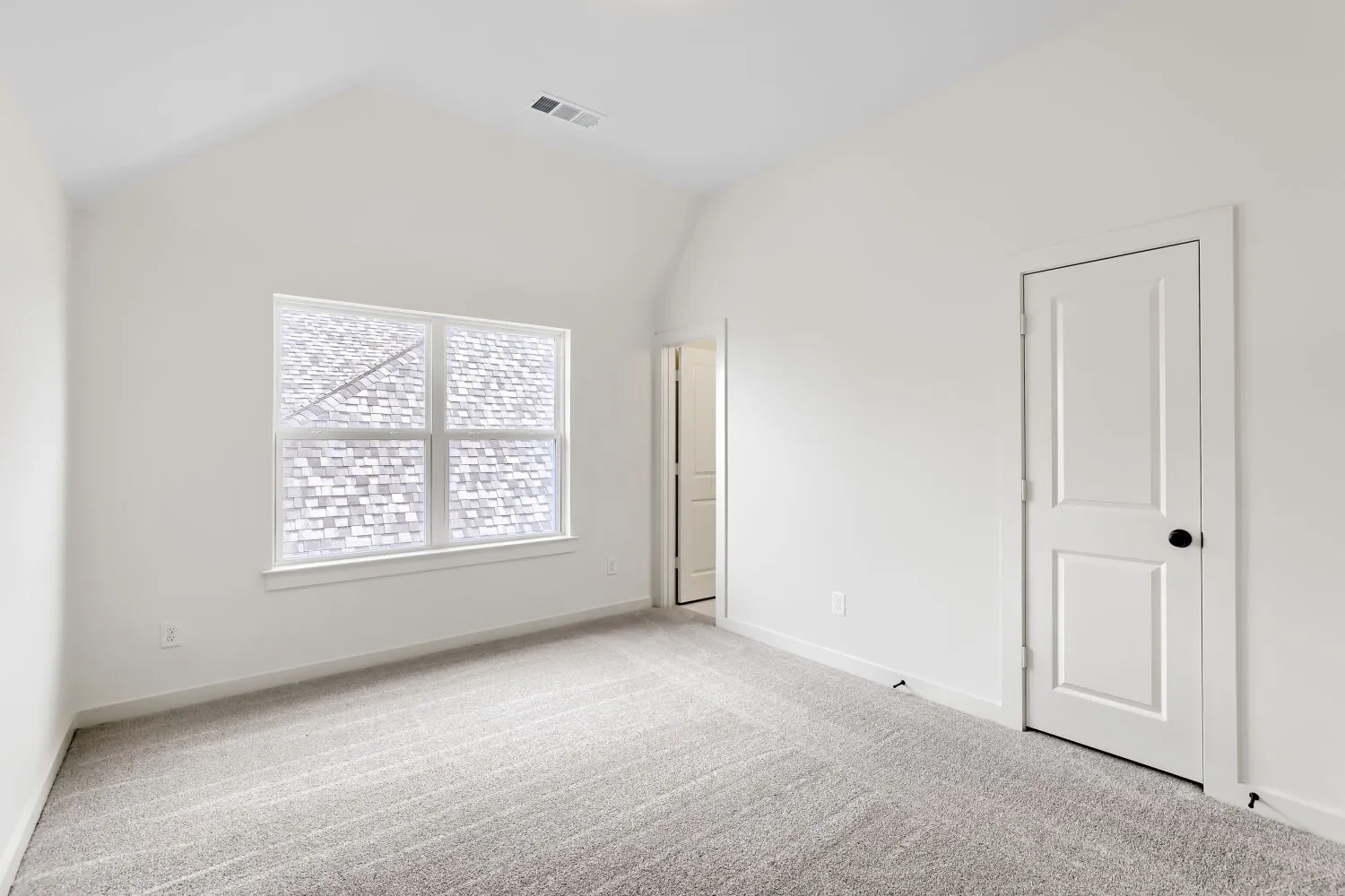 Vaulted ceiling, neutral wall paint, light-colored carpet, white trim, and two-panel interior doors