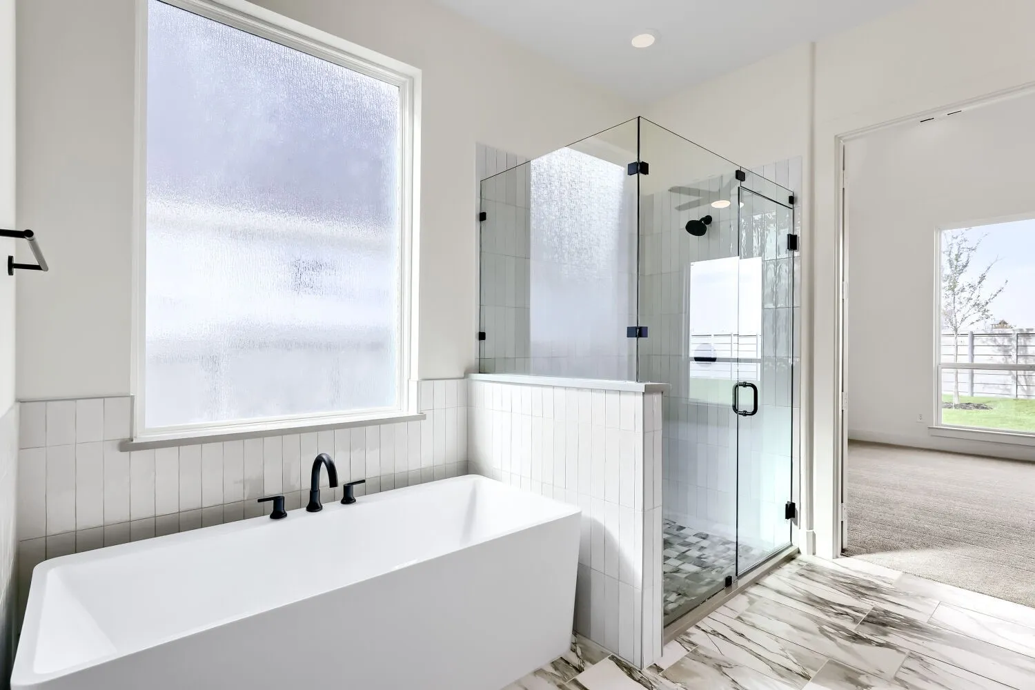 Freestanding soaking tub with matte black fixtures, glass-enclosed shower, white subway tile accents, and marble-look floor tiling