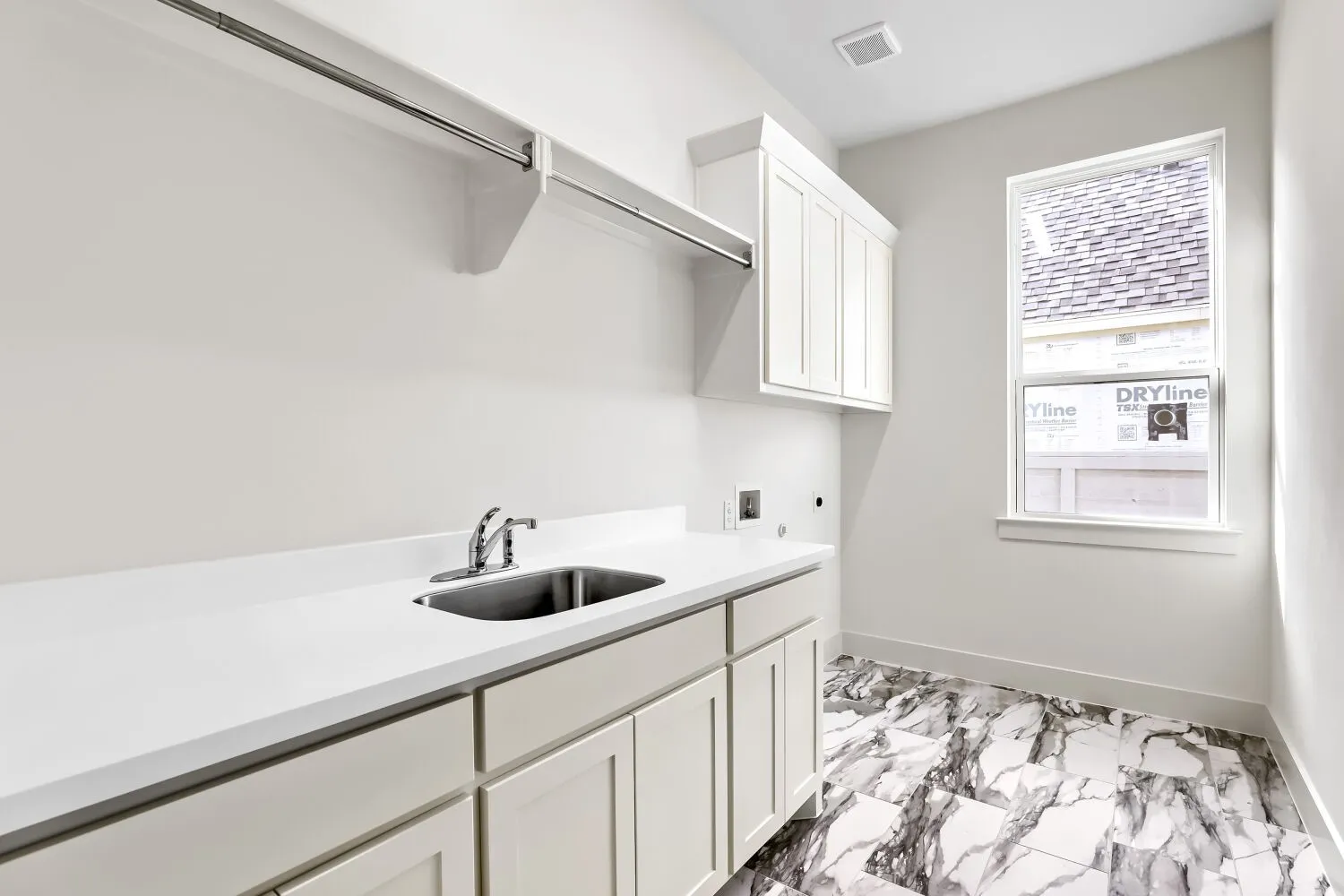 White shaker-style cabinetry, a built-in stainless steel sink, a spacious white countertop, a clothes hanging rod, and large format marbled flooring