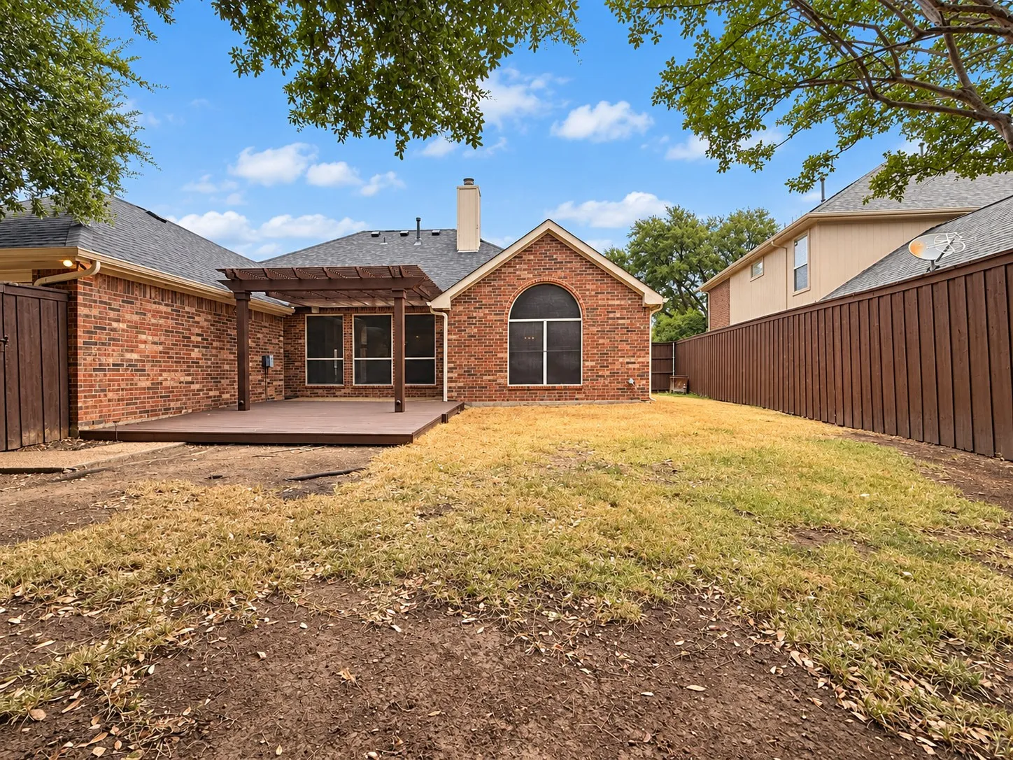 Brick exterior with an arched window, featuring a spacious deck with a pergola, and a private wood fence