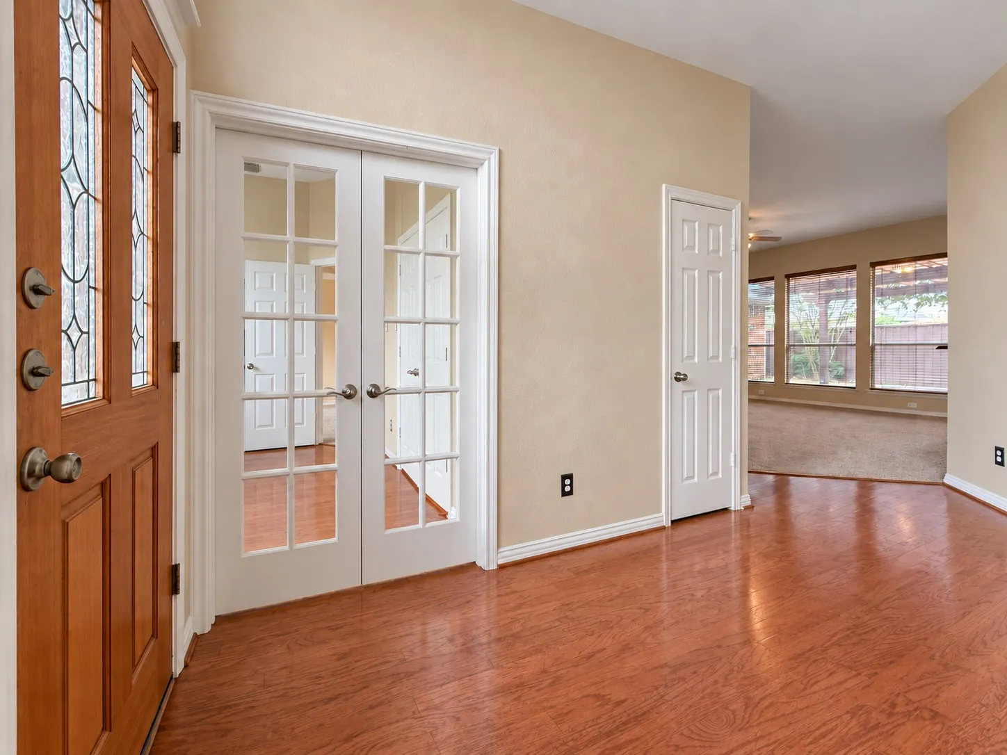 Wood-finish flooring, white trim, wood-paneled entry door with decorative glass inserts, and double French doors with glass panes