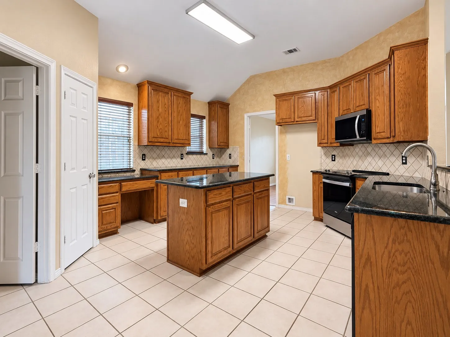 Kitchen featuring wood cabinetry, dark countertops, a central island, stainless steel appliances, and a tiled backsplash