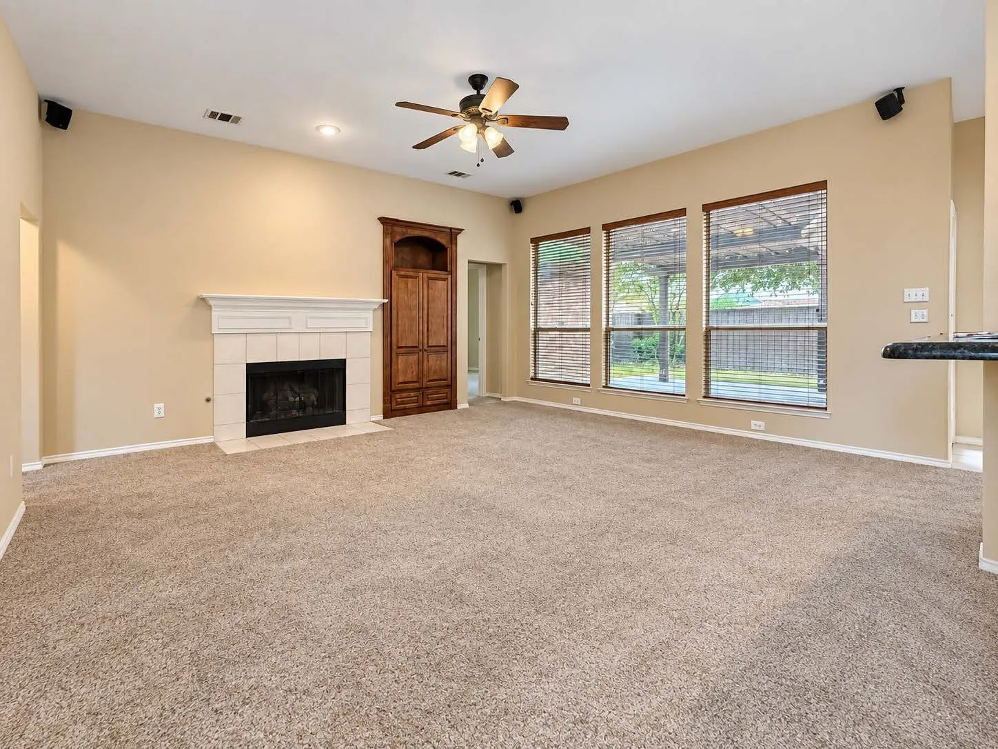 Living space featuring a tiled fireplace with a white mantel, built-in wood cabinetry, a ceiling fan, recessed lighting, and three large windows