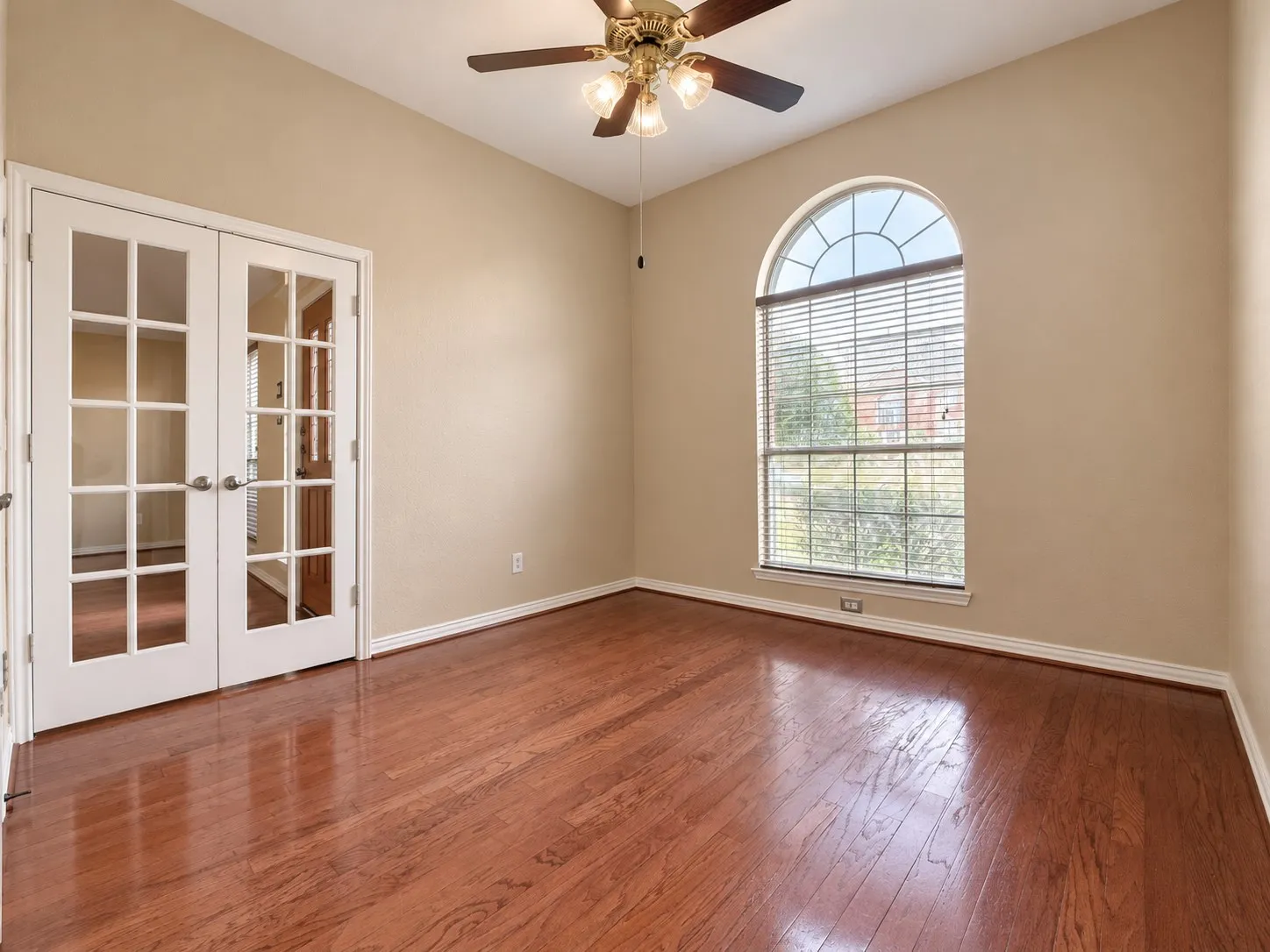 Hardwood flooring, arched window with blinds, double French doors, ceiling fan with light fixture, and light-colored walls