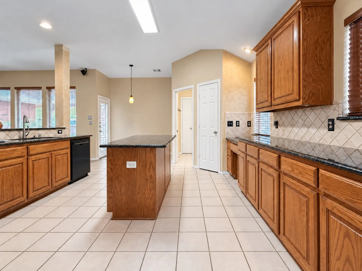 Kitchen featuring wood cabinetry, dark countertops, a central island, tile flooring, and a tile backsplash