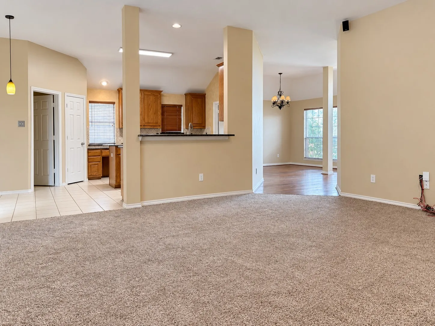 Carpeted living area with vaulted ceilings, featuring an integrated kitchen with wood cabinetry and tile flooring, and a separate dining area with wood-finish flooring and a chandelier