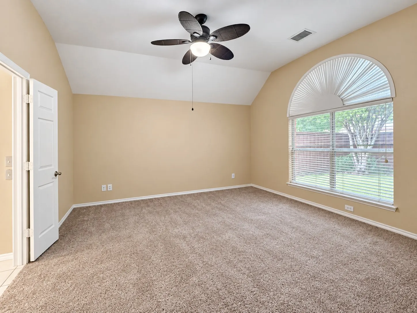 Vaulted ceiling room with textured carpeting, a ceiling fan, and a large arched window