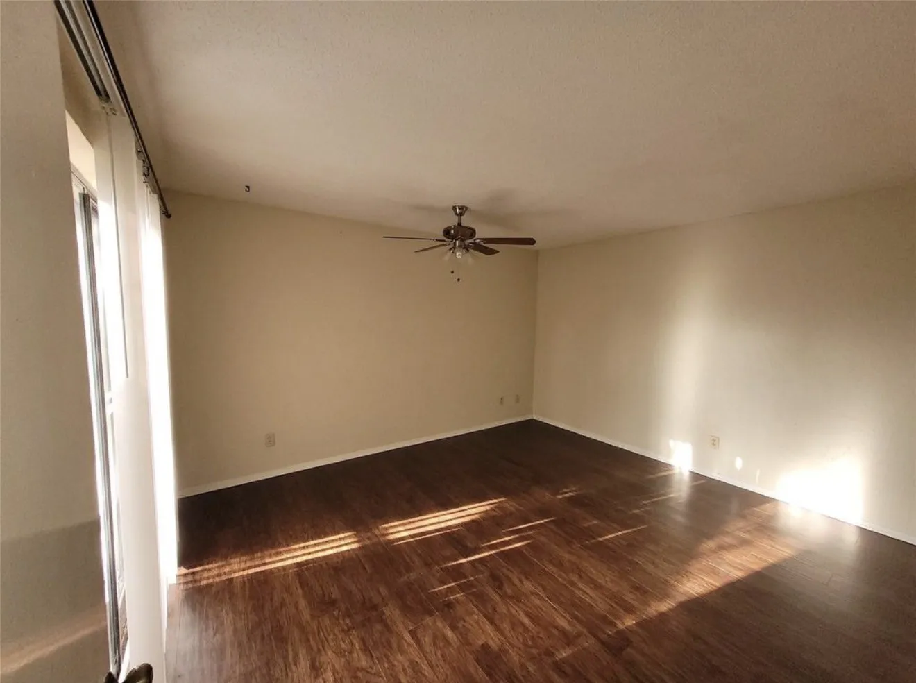 Spacious room featuring wood-finish flooring, light-toned walls, and a ceiling fan