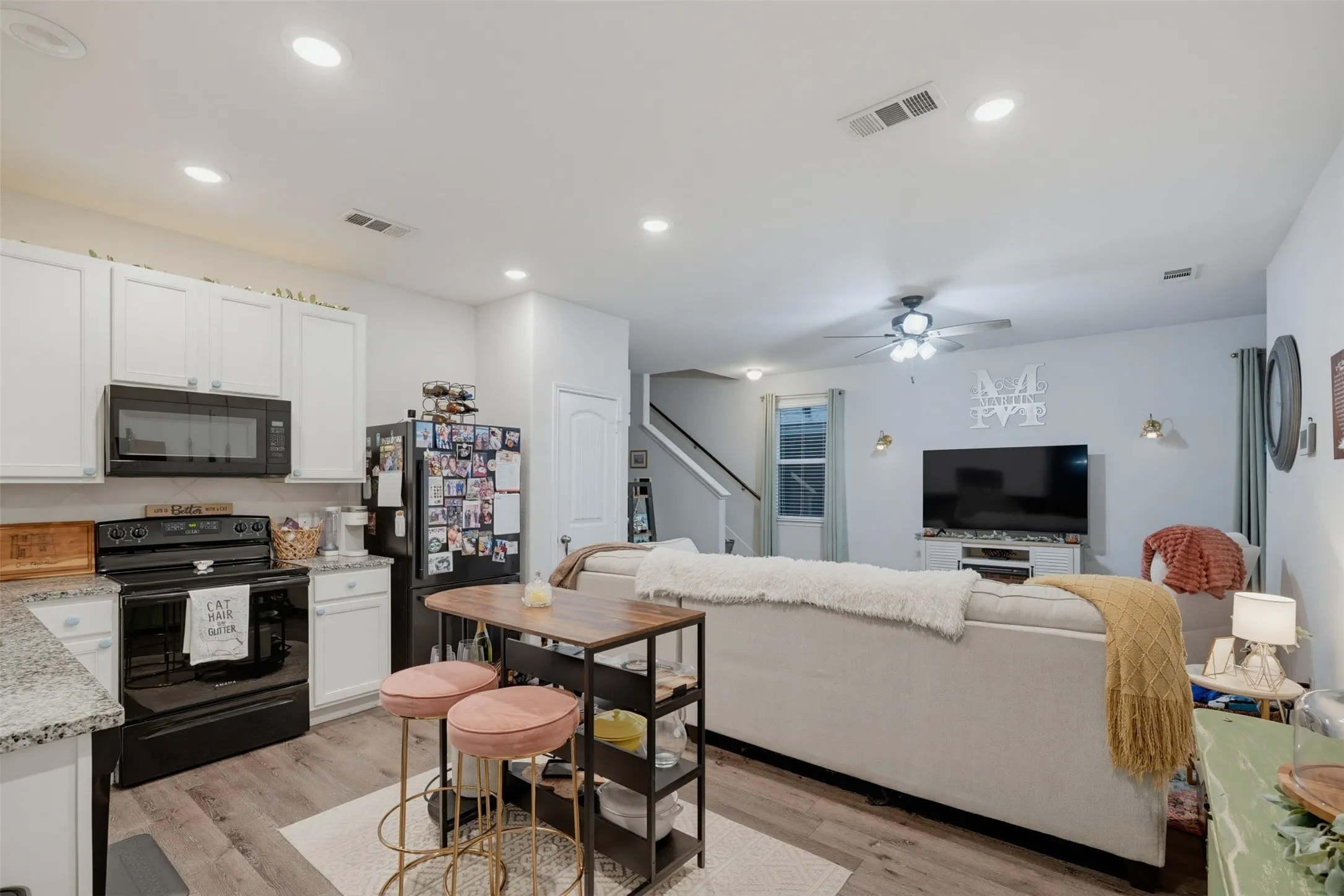 Kitchen featuring white cabinetry, black appliances, light-toned countertops, and wood-finish flooring