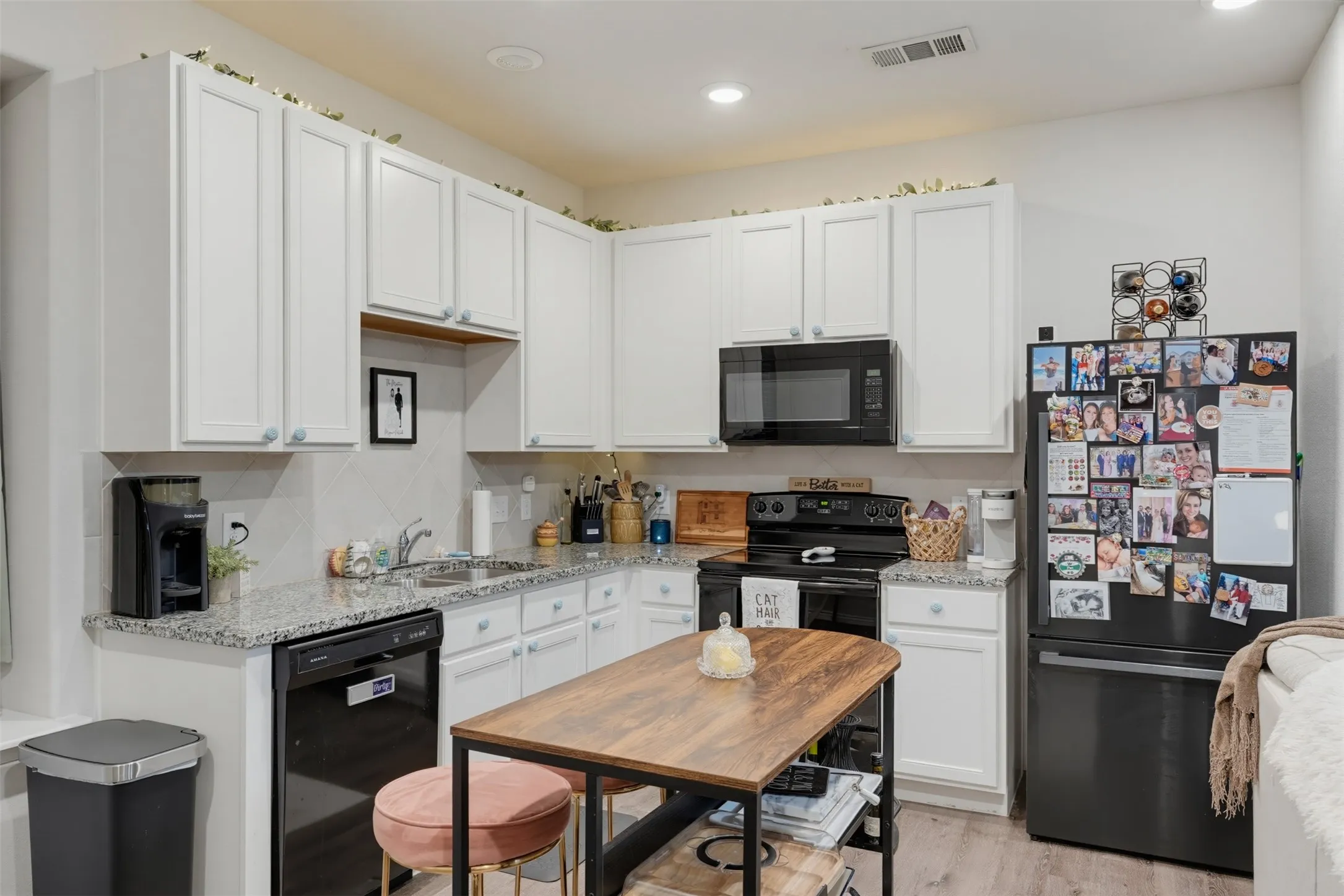 White cabinetry, granite countertops, black appliances, tile backsplash, and recessed lighting
