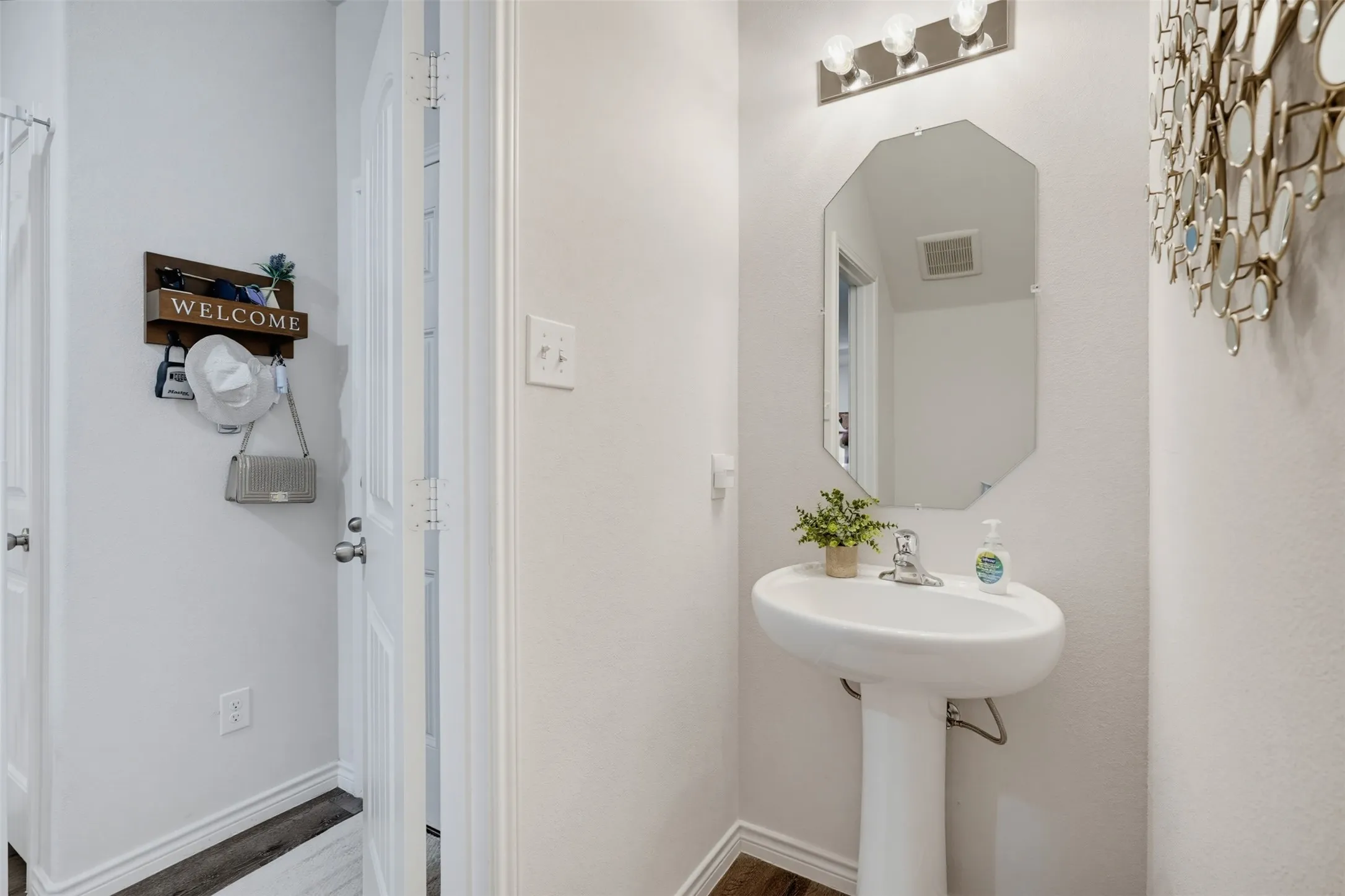 Pedestal sink with chrome faucet, classic octagonal mirror, and a three-light vanity fixture