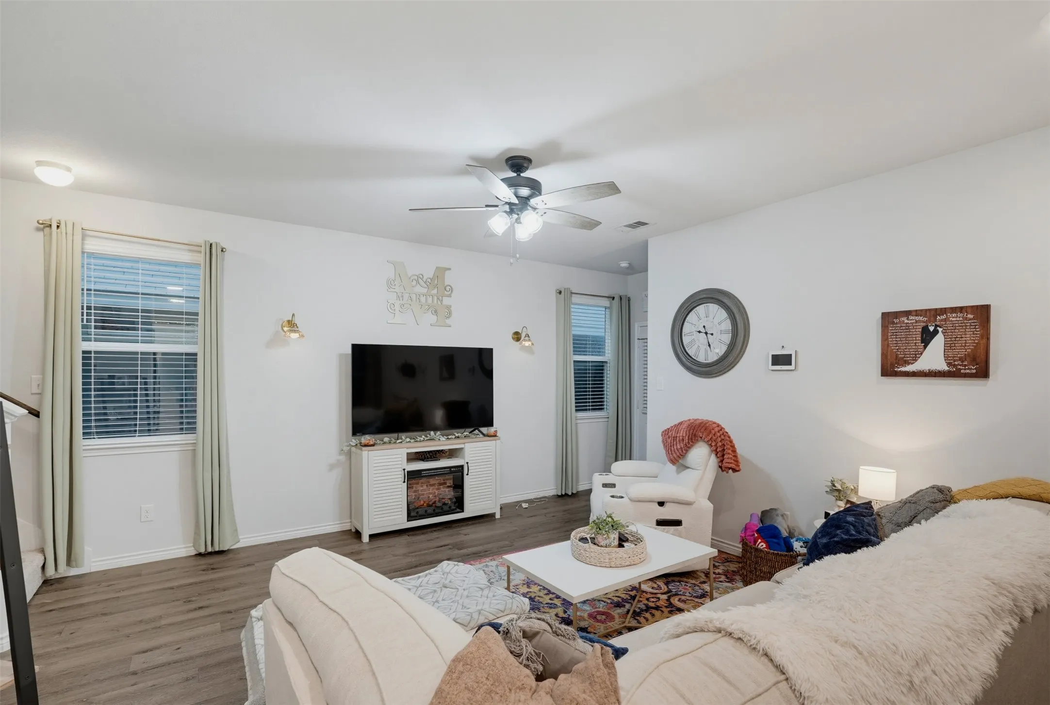 Open-concept living area featuring wood-finish flooring, white walls, and a ceiling fan with integrated lighting