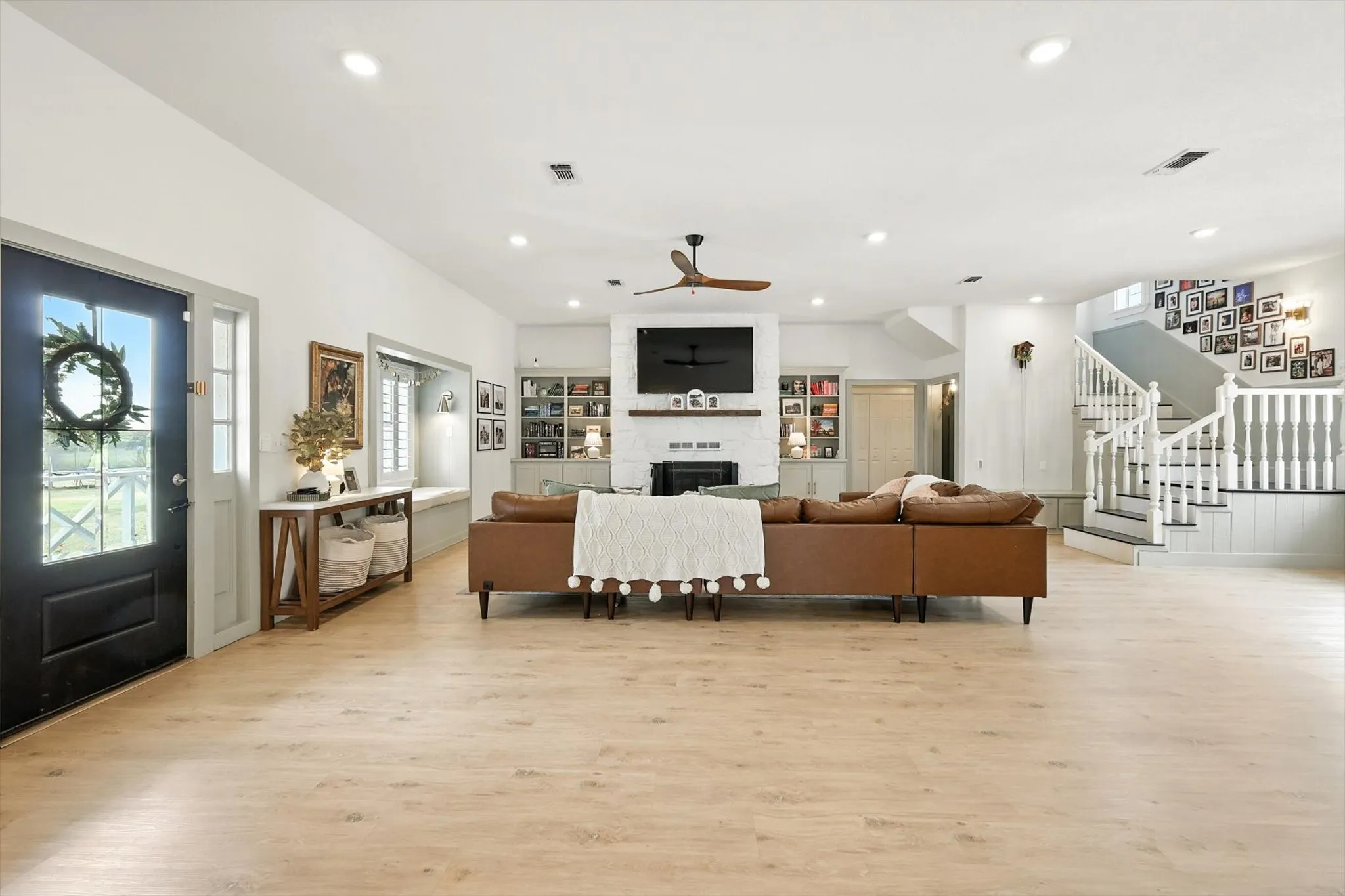 Light wood-finish flooring throughout, white painted walls, central fireplace with built-in cabinetry, and a white staircase with dark treads