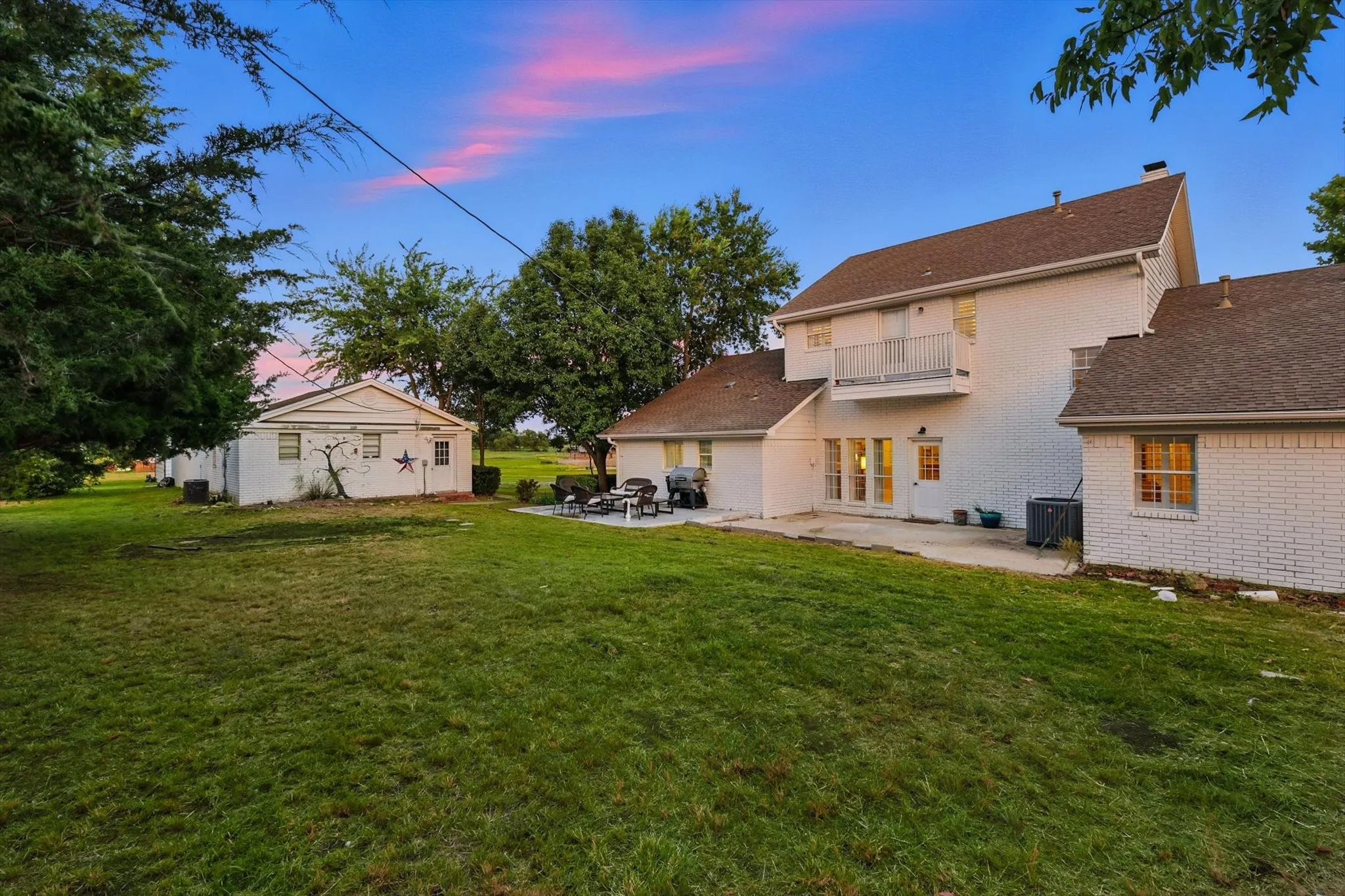 Expansive green lawn with a detached auxiliary building, concrete patio, and upper-level balcony