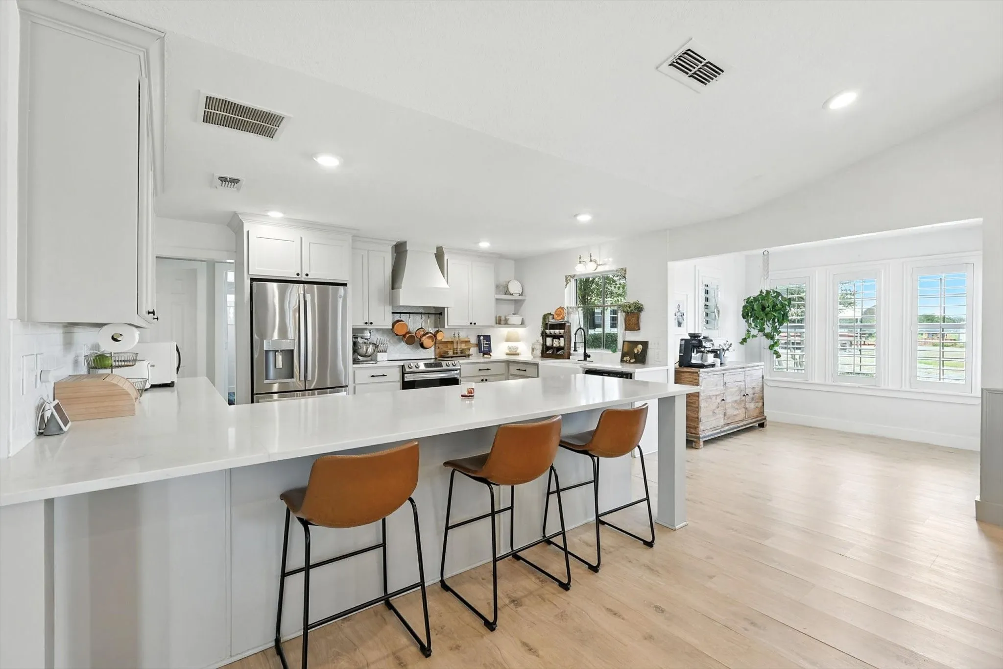 Kitchen featuring a large central island with seating, stainless steel appliances, white cabinetry, and light wood-finish flooring