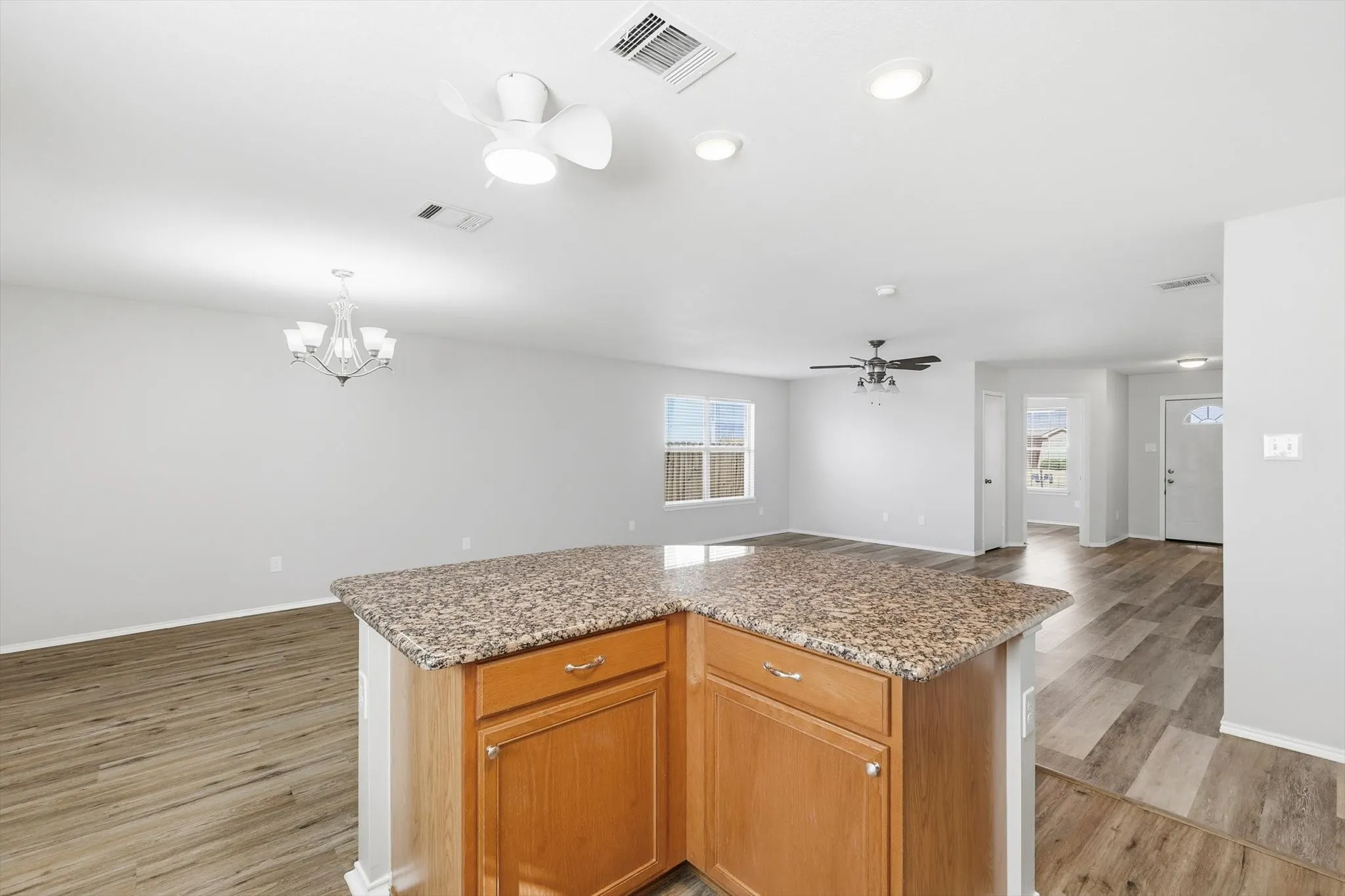 Kitchen island with wood-finish cabinetry and granite-style countertop, wood-finish flooring, recessed lighting, ceiling fan, and chandelier