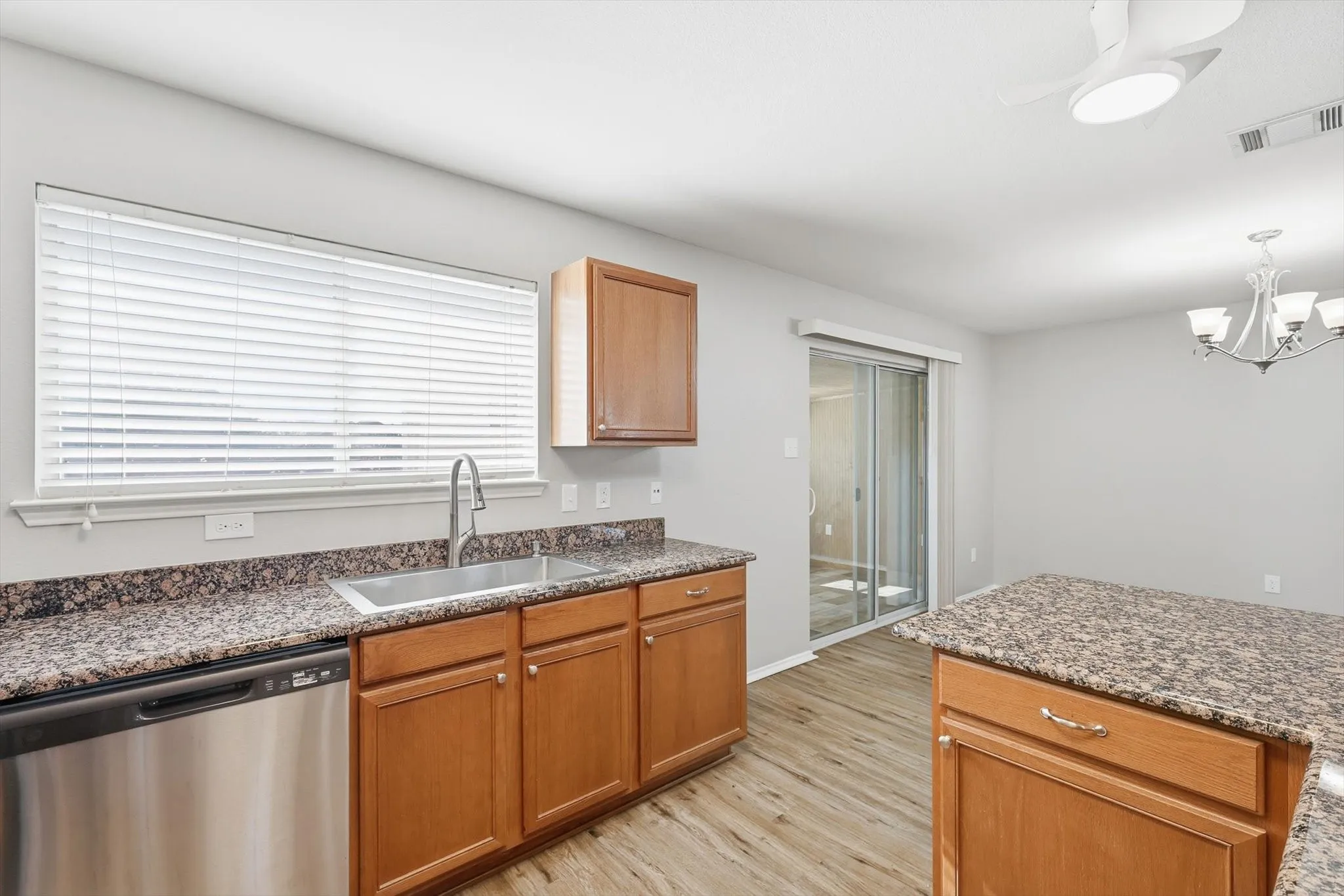 Kitchen featuring wood-finish flooring, granite countertops, wood cabinetry, a stainless steel dishwasher, and a stainless steel sink with a high-arc faucet
