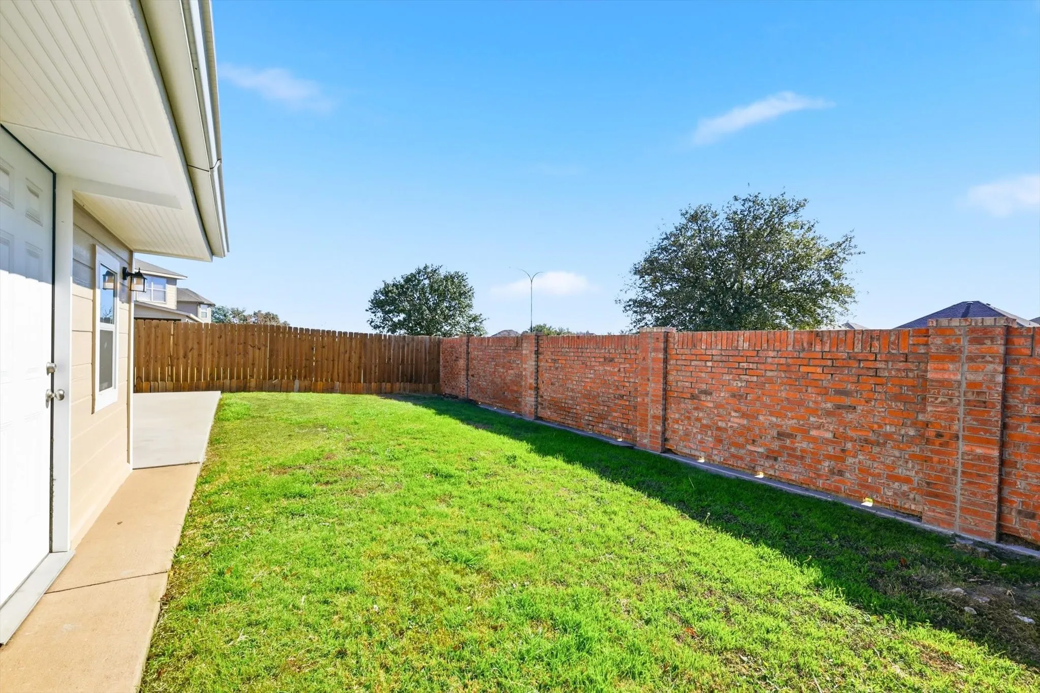 Manicured lawn with a brick perimeter wall, wood privacy fence, and concrete patio