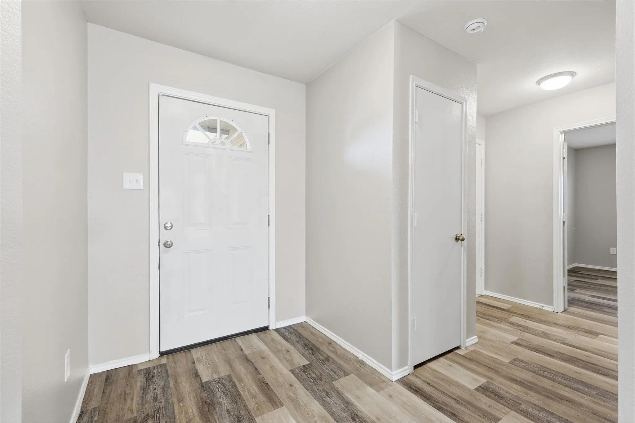 Entryway with wood-finish flooring, a paneled door with an arched window, and neutral wall tones